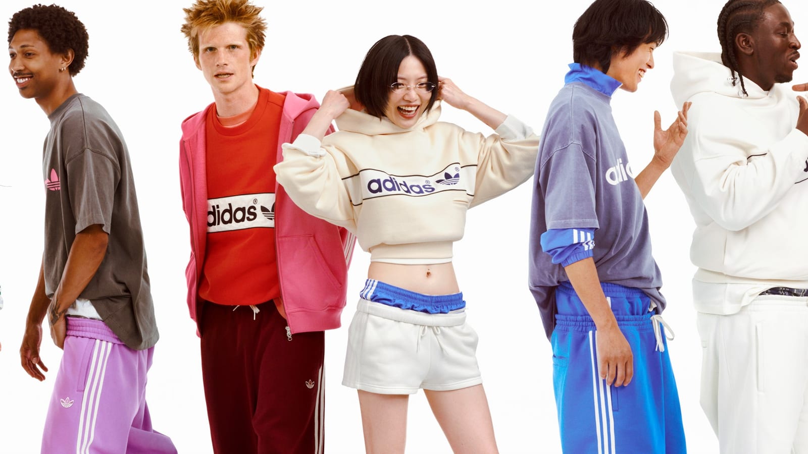 Five models against a white background in adidas sweats: a lilac track pant, a pink zip hoodie over a red adidas sweatshirt, a cream cropped adidas hoodie with white shorts, a blue track top and pant, and a white hoodie