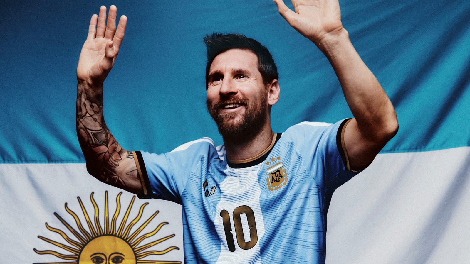 Lionel Messi waving in adidas's Argentina Messi Special Edition jersey, sky blue and white with gold details and the number 10, in front of the Argentine flag