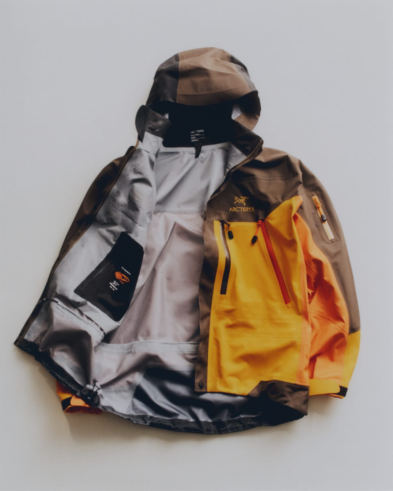 The ARC'TERYX x BEAMS Theta AR jacket laid open, color-blocked in brown, orange and yellow, with a grey GORE-TEX lining