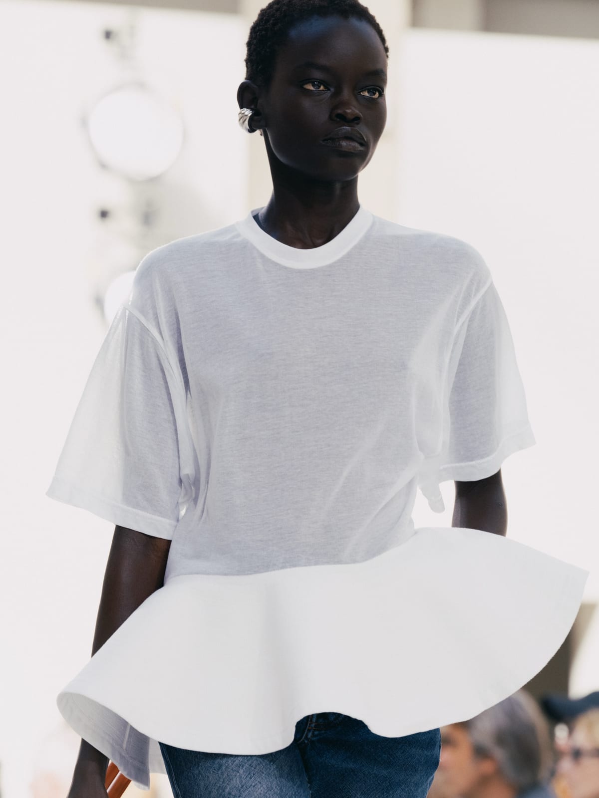 A model in a loose white T-shirt with a flared white peplum hem, worn over jeans