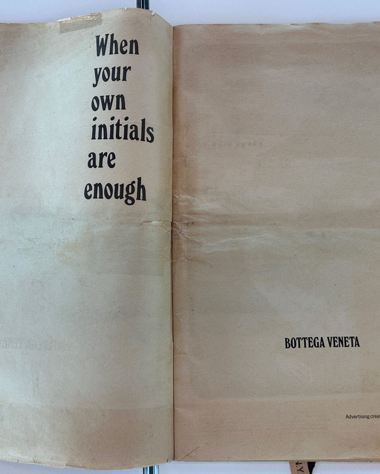A yellowed, creased magazine spread with the words When your own initials are enough set in black serif type at the top of the left page and the Bottega Veneta name printed small at the bottom right