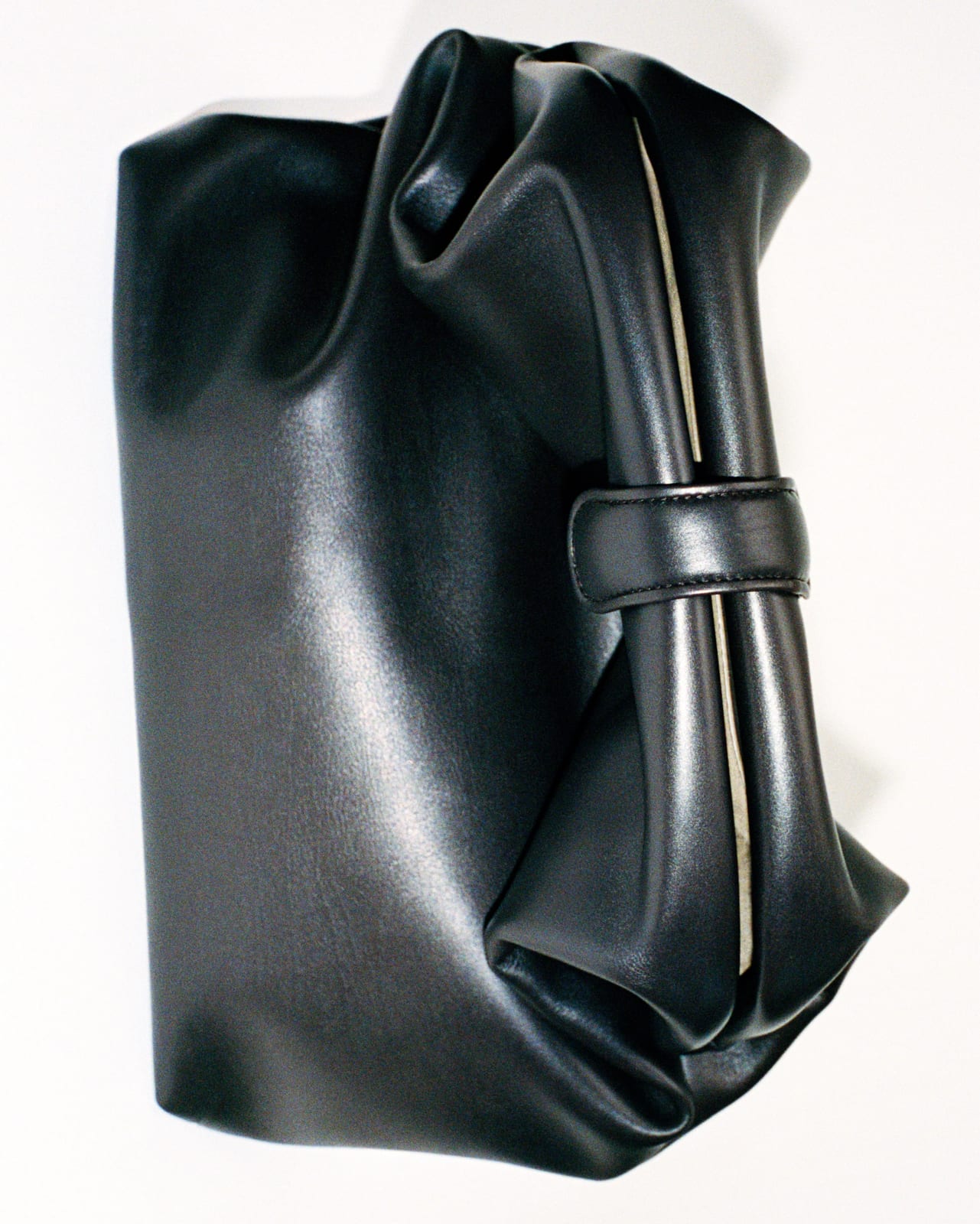 A soft black leather handbag with a rolled handle held by a leather loop, photographed on a white background