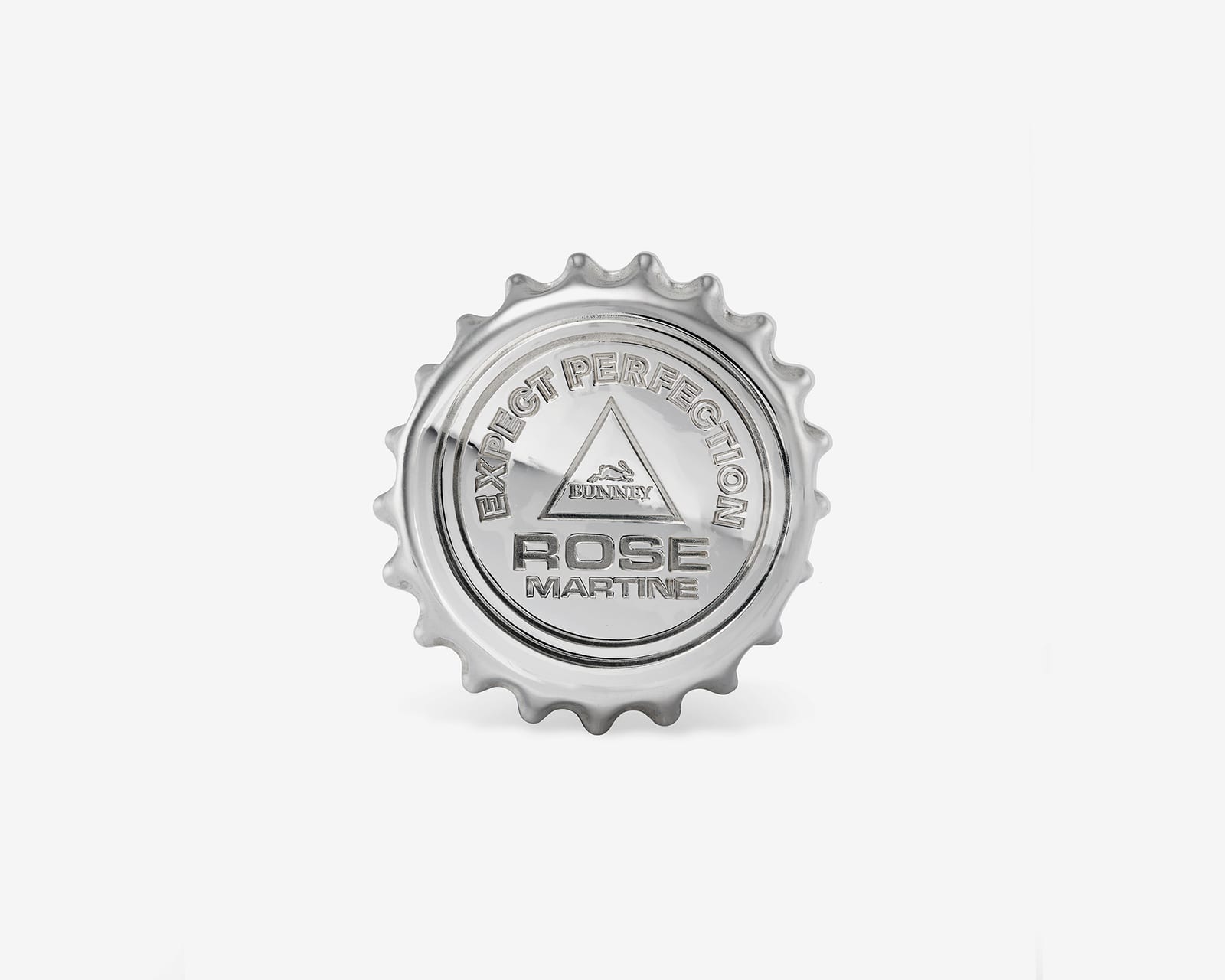 A sterling silver badge shaped like a crimped bottle cap, embossed with EXPECT PERFECTION around a triangle holding the Bunney logo, and ROSE MARTINE beneath, on a pale grey background