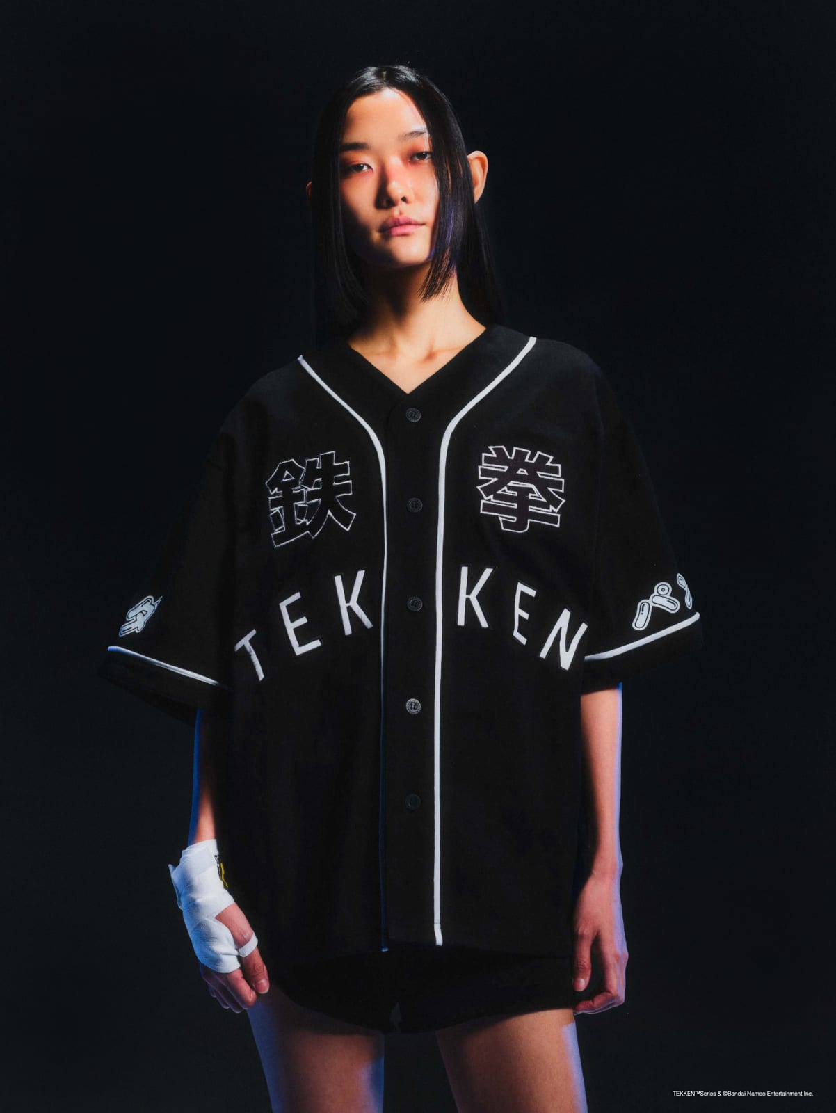 A model in the black Carnival x Tekken baseball jersey, with 鉄拳 on the chest and TEK KEN spelled across the button placket