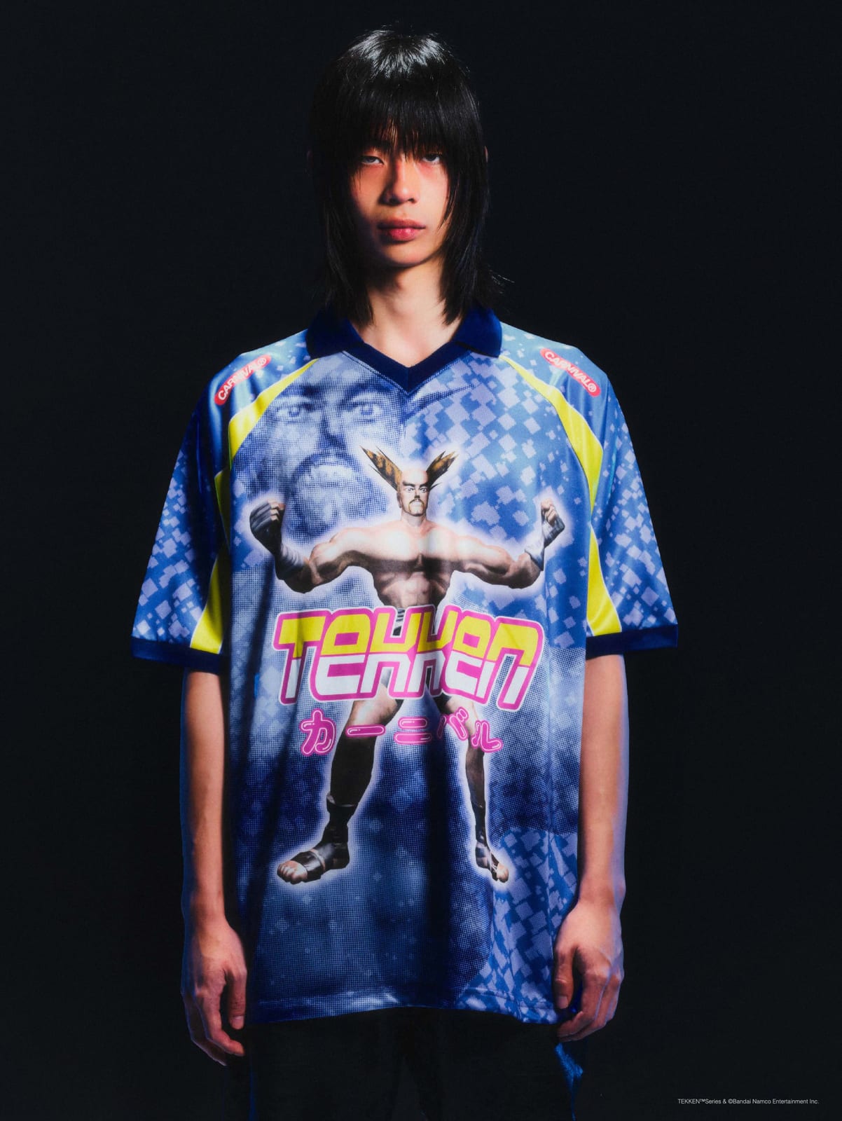 A model in the blue, all-over-print Carnival x Tekken football jersey, with a fighter across the front, Tekken in pink and カーニバル underneath