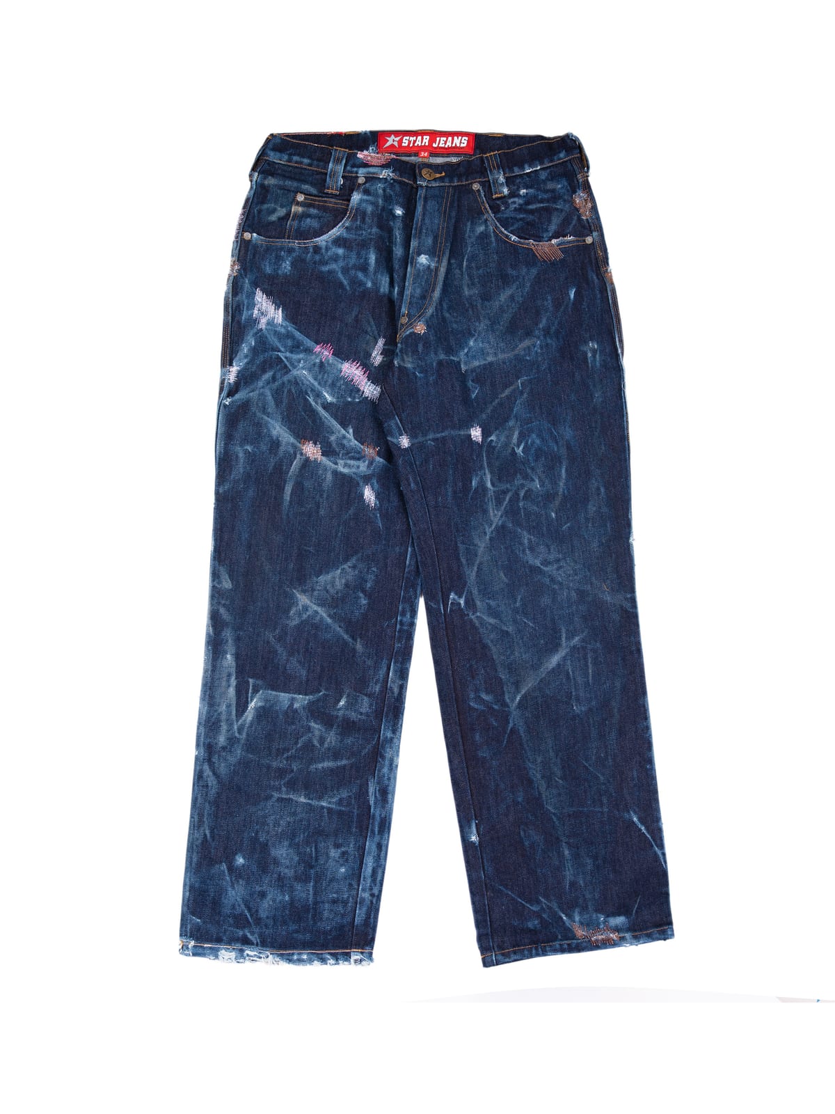 A pair of dark indigo straight-leg jeans laid flat on white, heavily streaked with pale bleach marks, with frayed hems, small pink darned patches and a red C-Star Jeans tag at the waistband