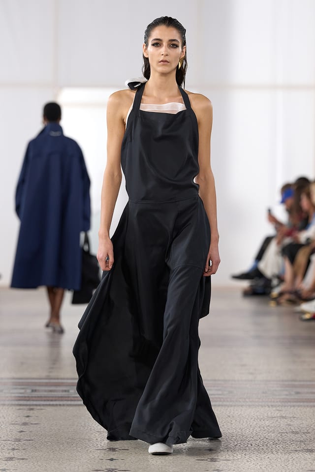 A model in a black halter-neck apron dress with a wide, full skirt