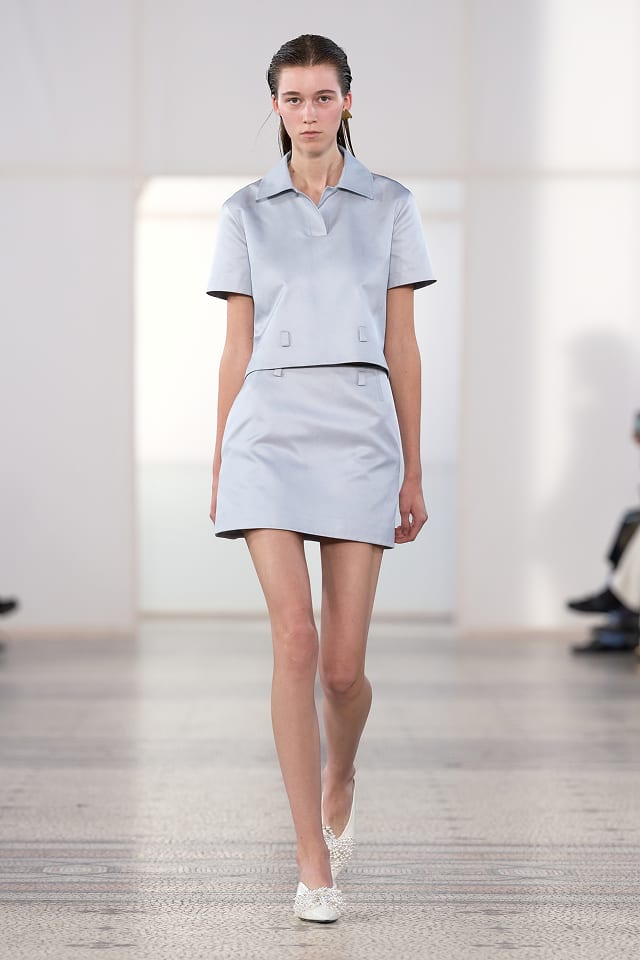 A model on Carven's pale runway in a light blue short-sleeved satin jacket and matching mini skirt, with white shoes