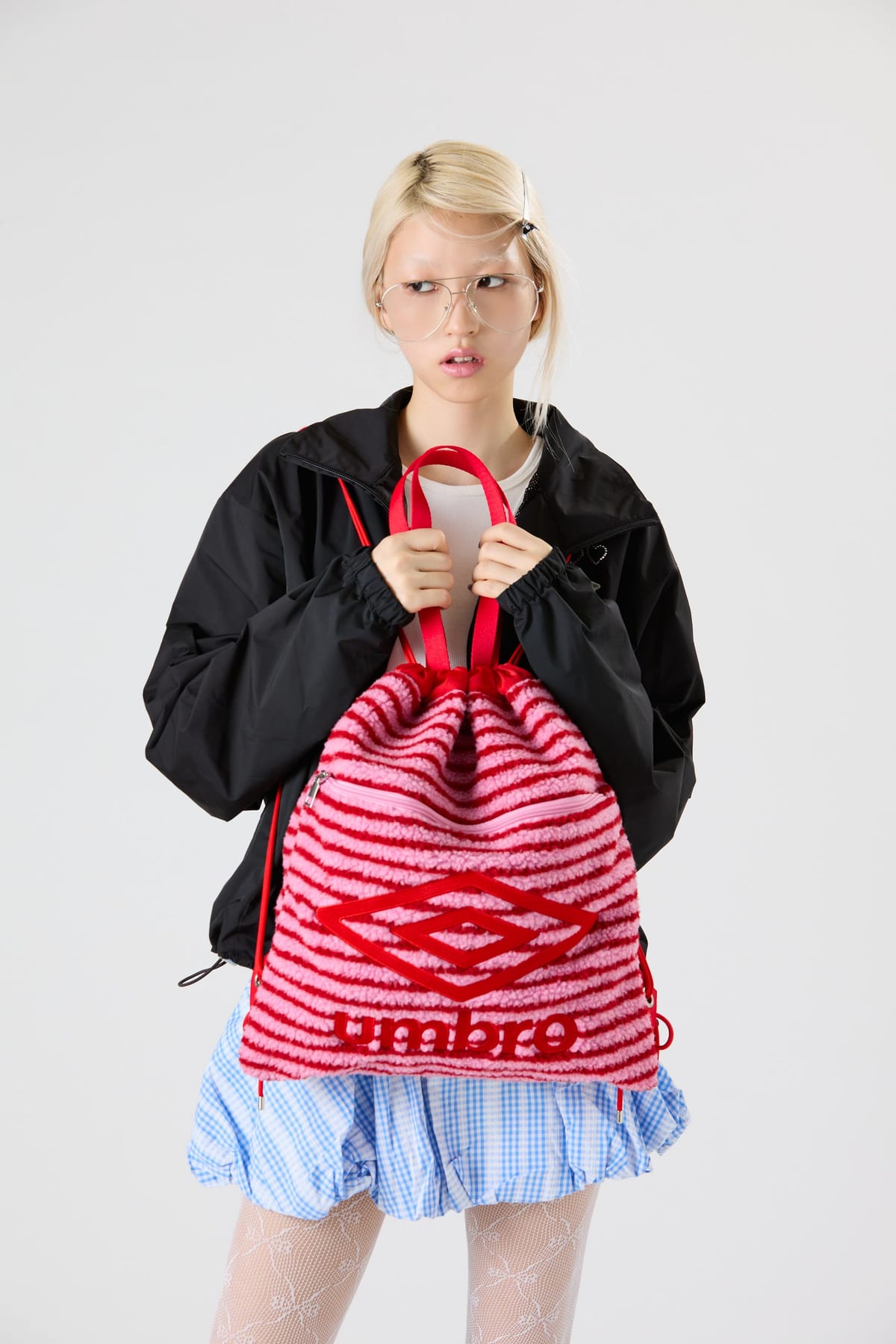 A model in a black jacket carrying a red and pink striped fluffy Umbro drawstring knapsack by its handles