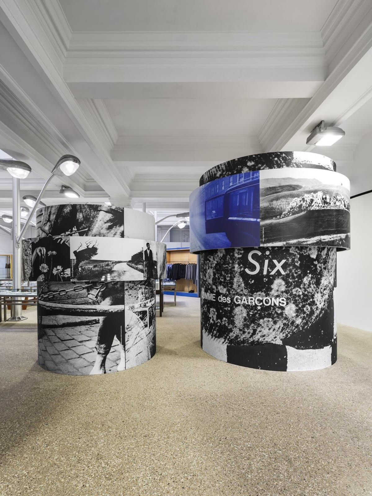 Inside Dover Street Market London, round pillars wrapped in collaged black-and-white and blue photographs, with Six COMME des GARÇONS printed on one and a shop floor stretching behind