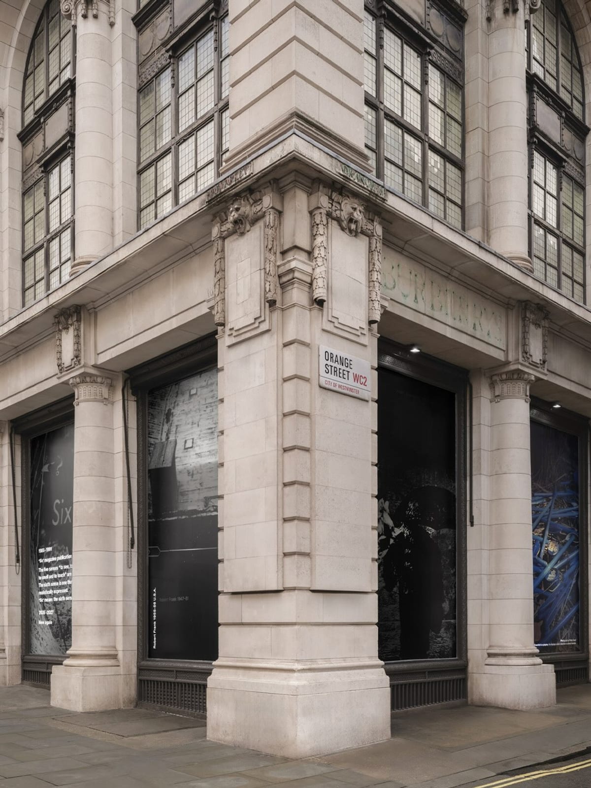 The stone corner of Dover Street Market London, an Orange Street sign on the wall, its tall windows covered in large black-and-white and blue photographs from Six