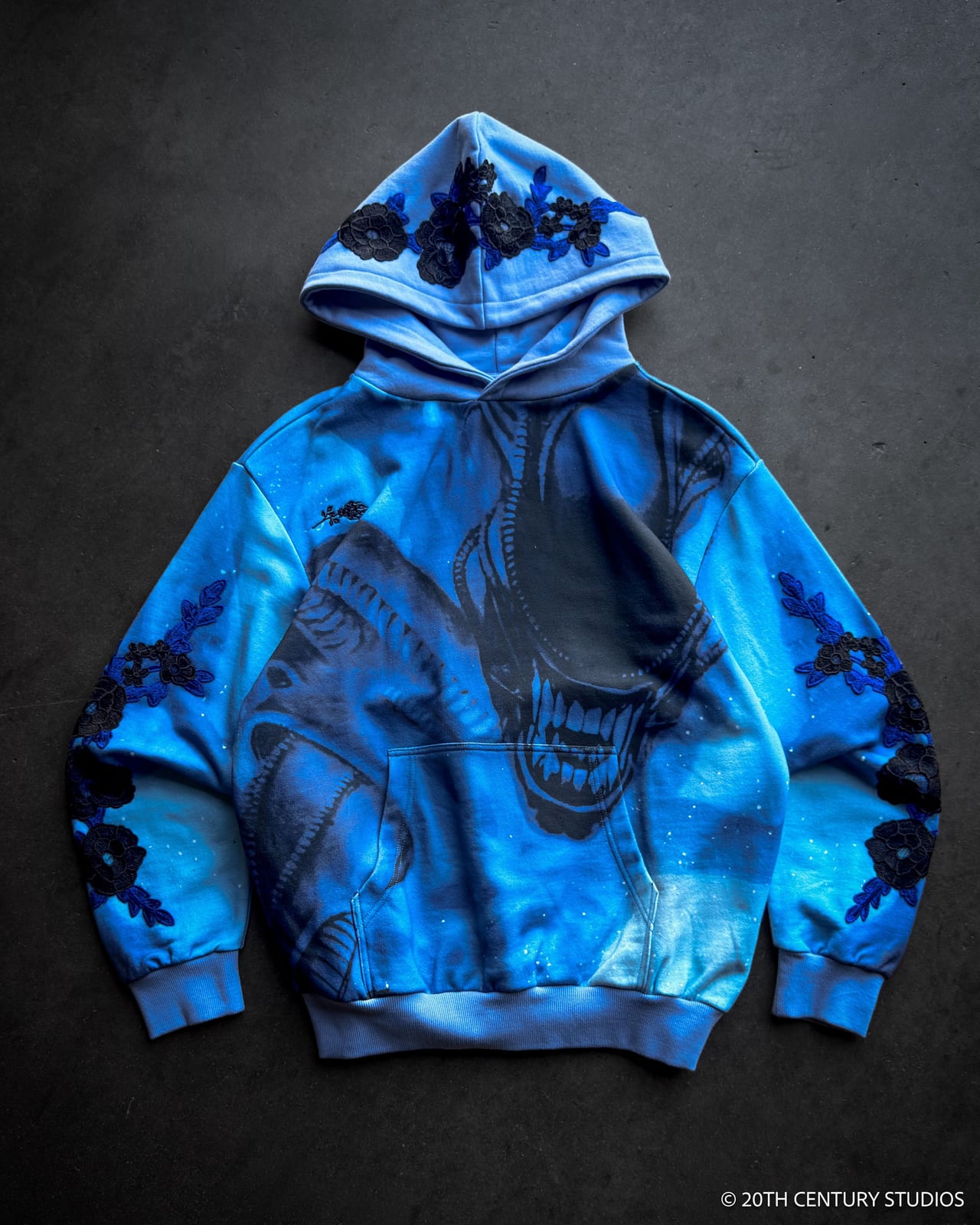 A blue Civil Regime hoodie printed all over with a xenomorph from Alien in marbled blue, with black rose appliqués on the hood and sleeves