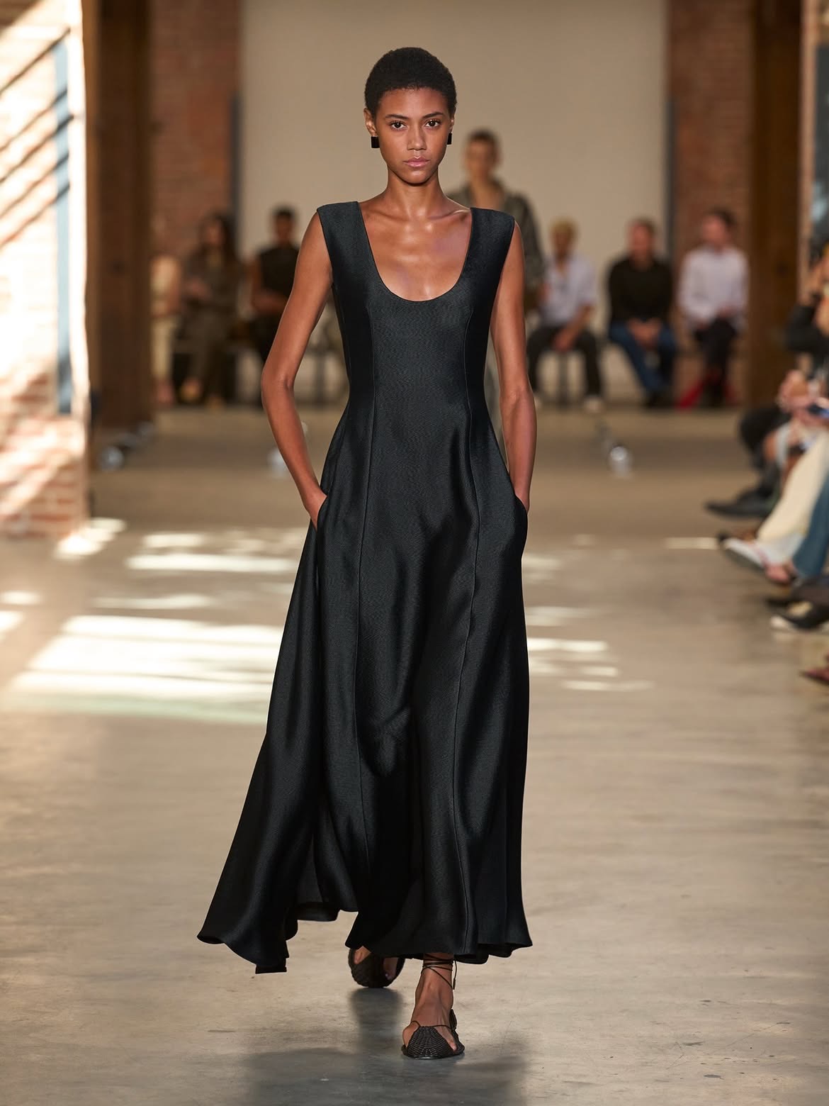 A model in a long black sleeveless dress with a scoop neck and a full, flared skirt