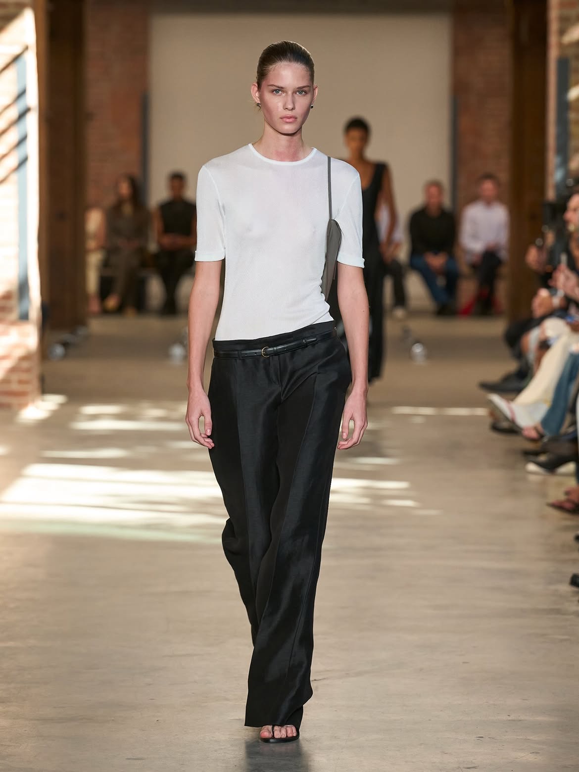 A model in a fitted white short-sleeve knit tee and black wide-leg trousers with a thin black belt