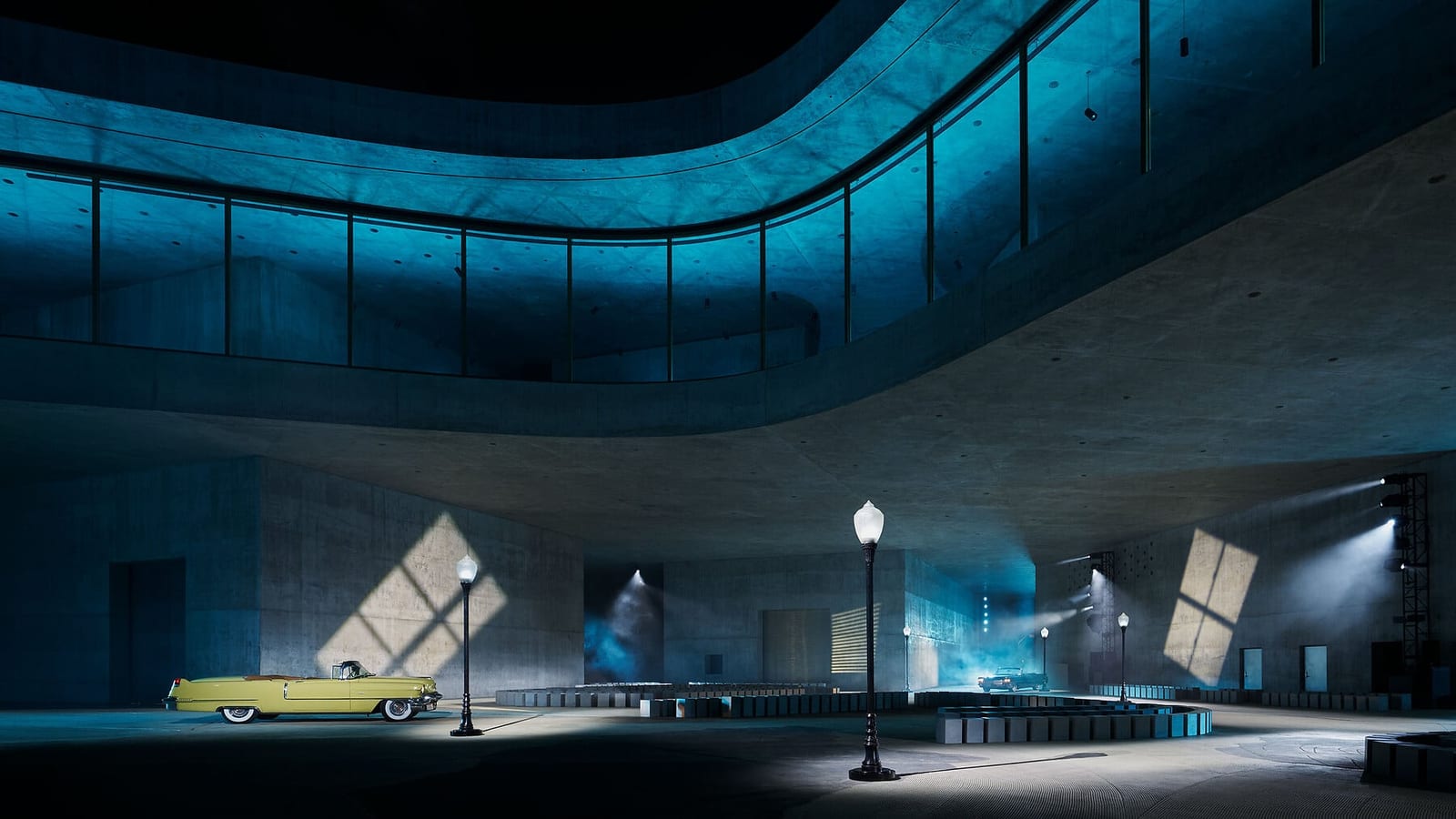 The set of Dior's Cruise 2027 show at LACMA in May: Peter Zumthor's new concrete wing lit blue at night, with a yellow vintage convertible and streetlamps on the plaza beneath it