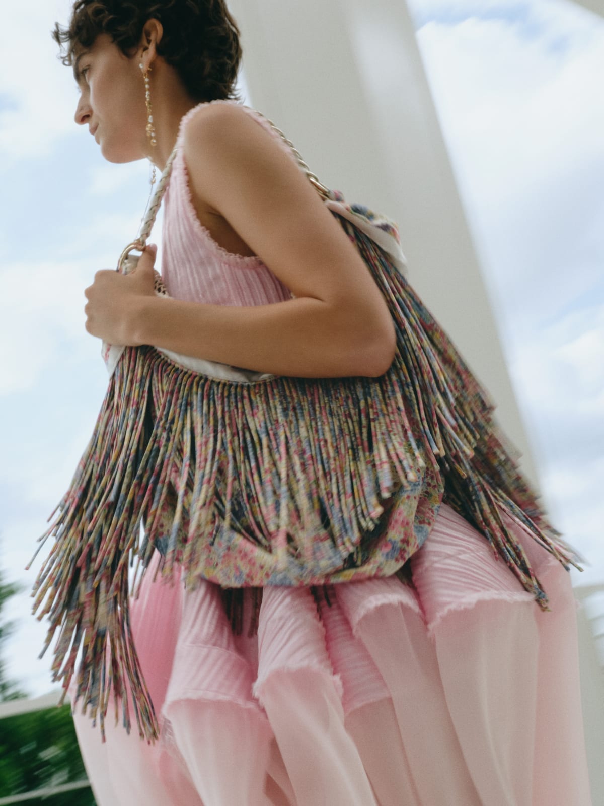 A Dior Summer 2027 look with a pleated pink top and flounced skirt, carrying a long fringed shoulder bag