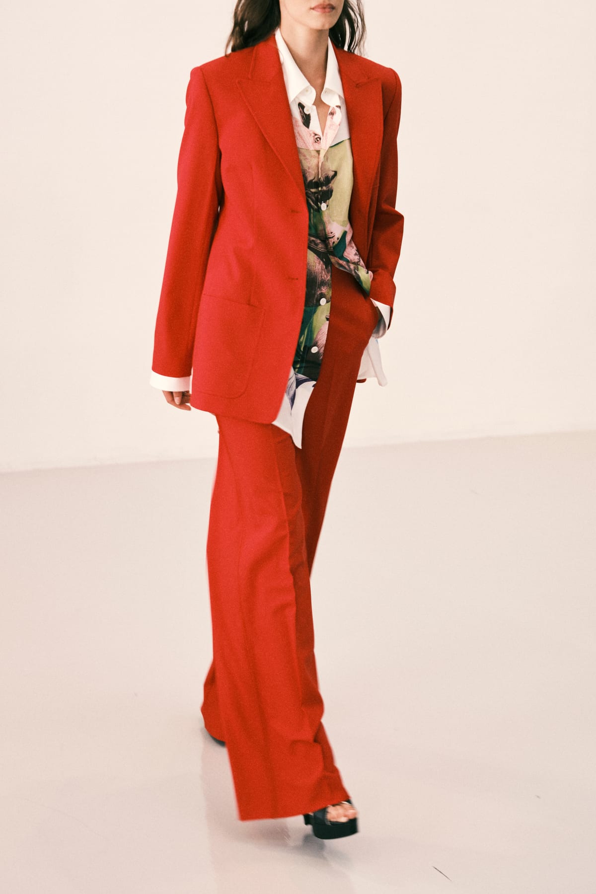 A model in a red suit with a long jacket and wide trousers over a printed shirt, from the Diane von Furstenberg Spring 2027 collection