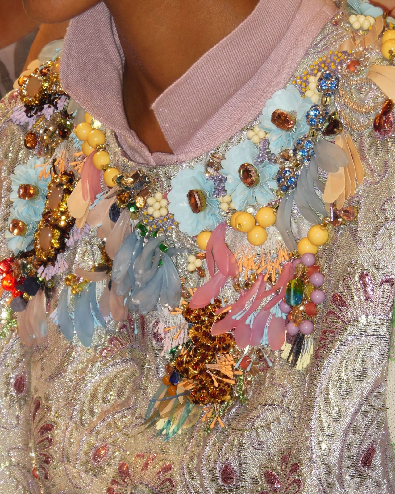 Close-up of a Dries Van Noten Spring/Summer 2027 look: a silver brocade top with a pink collar, covered at the neckline in beaded flowers, sequin petals, crystals and yellow beads