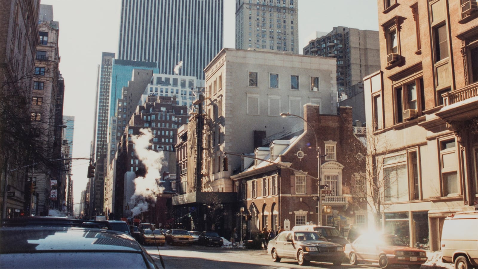An archive photo of a sunlit Madison Avenue in winter, with yellow cabs, steam rising from the street, snow at the curb and an ETRO awning in the distance below a pale stone building