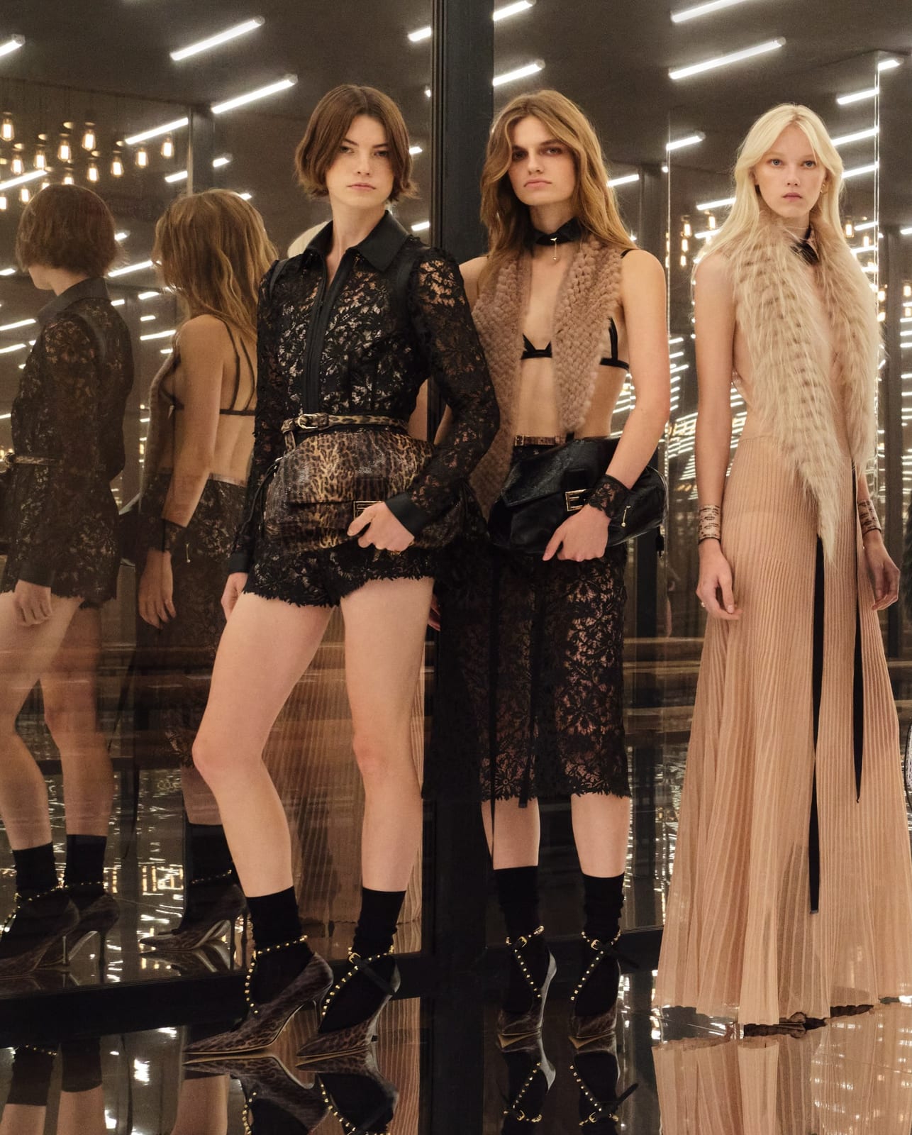 Three Fendi Spring 2027 looks on the mirrored runway: black lace over a bra and shorts, a sheer skirt worn with a bra and belt, and a long pleated cream gown