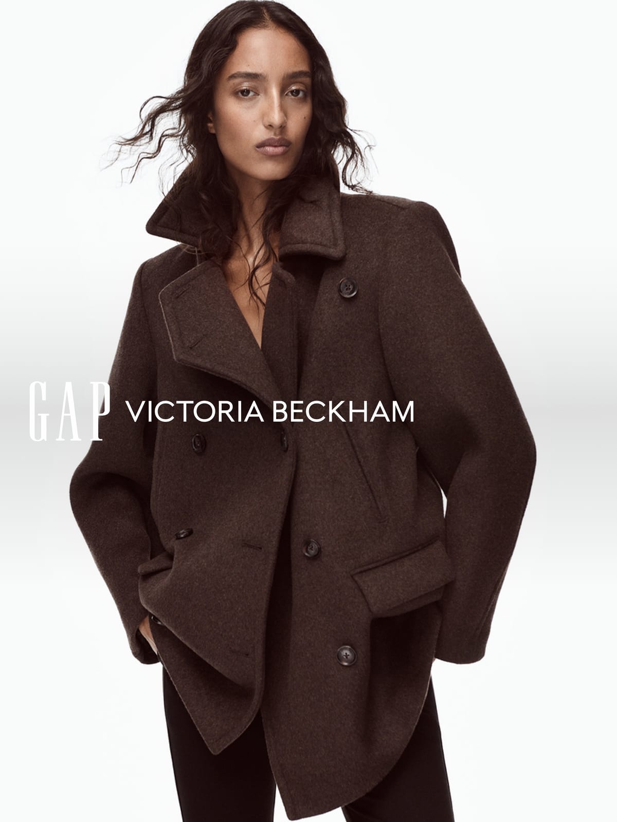 Mona Tougaard in an oversized double-breasted dark brown wool jacket with a wide collar and flap pockets, against a white backdrop with the Gap and Victoria Beckham logos