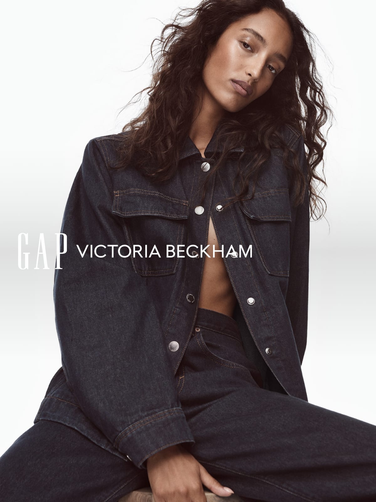 Mona Tougaard in a dark rinse oversized denim shirt jacket worn open, with matching dark jeans, against a white backdrop with the Gap and Victoria Beckham logos