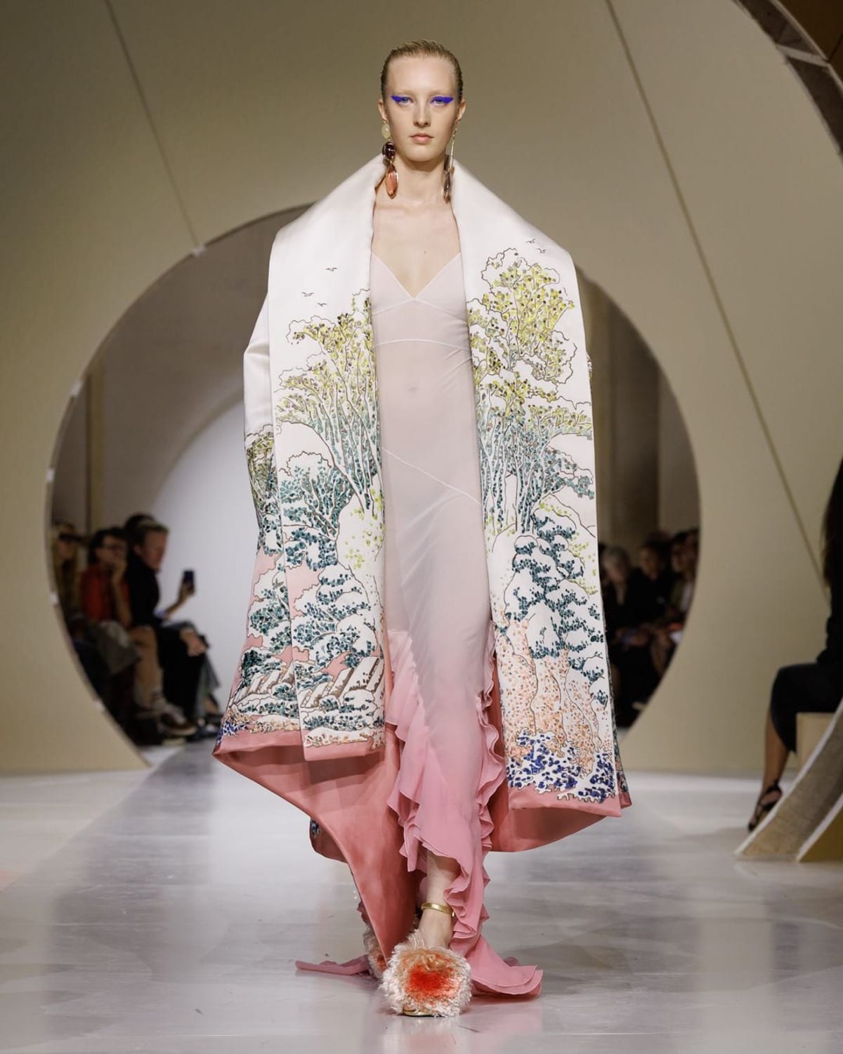 A model in a long pale pink robe with a pattern embroidered across it, worn open over a sheer slip