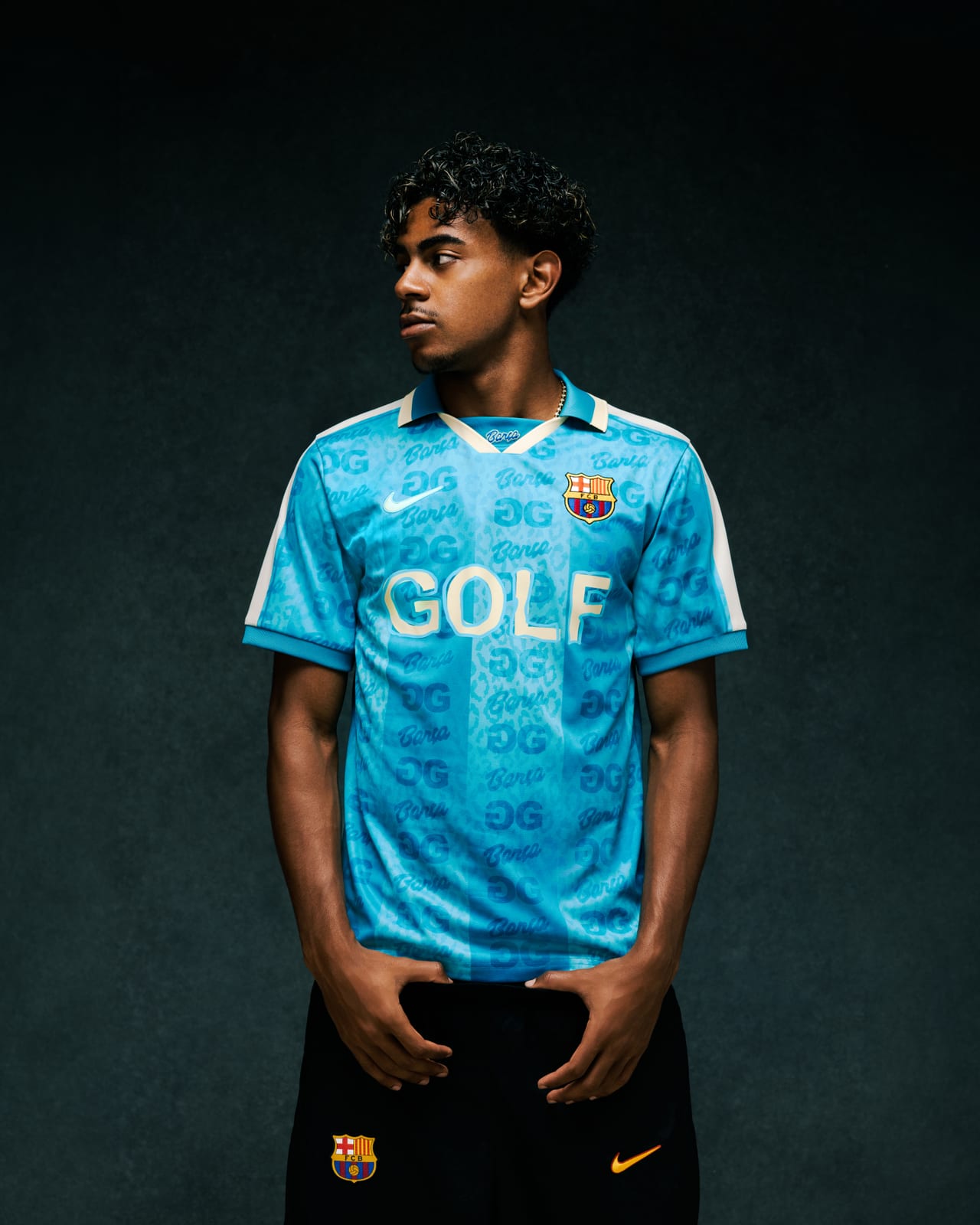 Lamine Yamal against a dark backdrop in GOLF WANG's teal short-sleeve FC Barcelona jersey with a cream collar and shoulder panels, cream GOLF lettering, the club crest, a white Nike Swoosh and an all-over leopard and logo pattern, worn with black shorts carrying the crest and an orange Swoosh