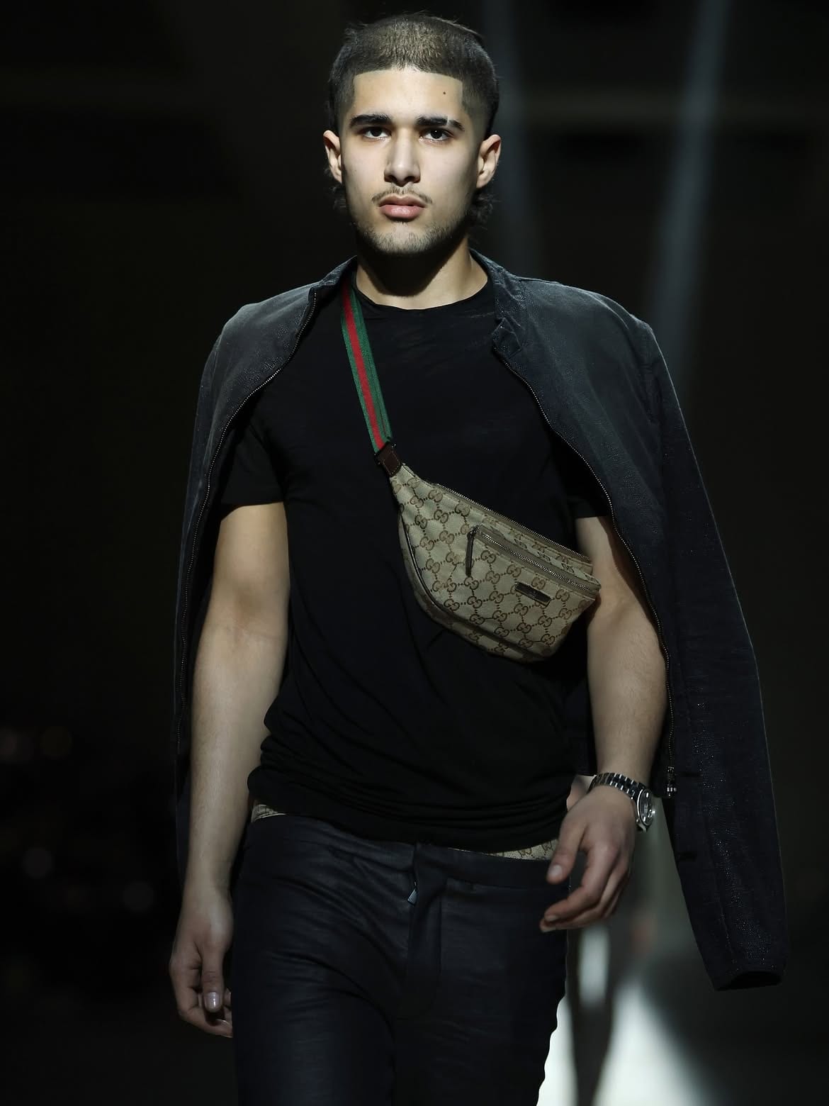 A model at Demna's first Gucci show in a black tee, with a black jacket over the shoulders and a GG canvas belt bag on a green and red Web strap