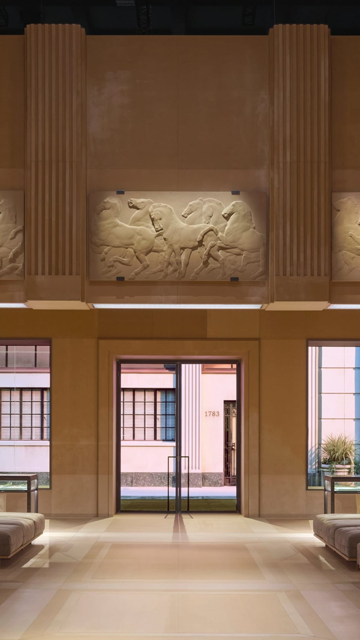 Gucci's Store Show set in Milan: a stone-coloured room with a bas-relief of galloping horses, fluted pilasters, display cases and low benches
