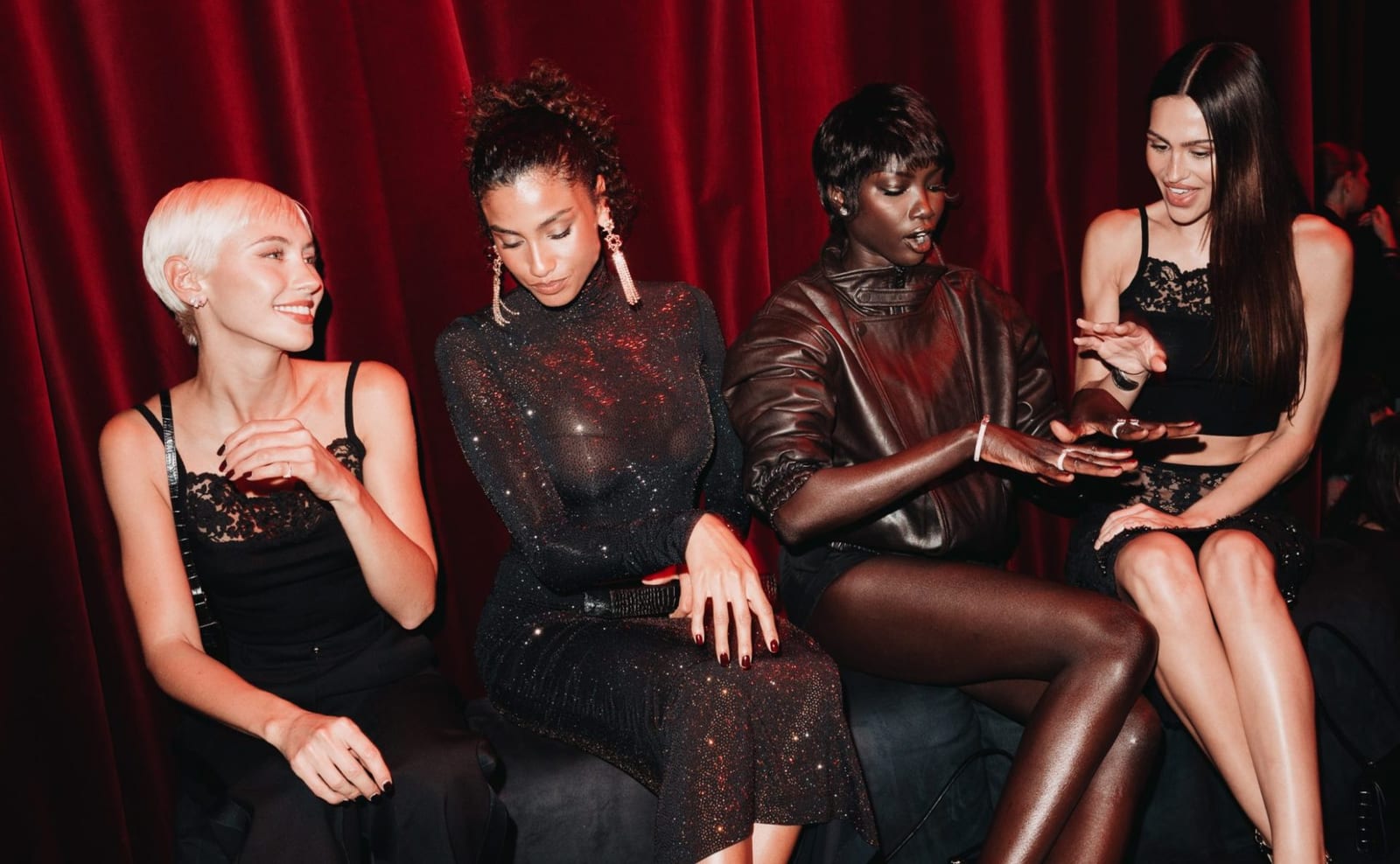 Four guests at the ELIE SAAB H&M launch party at the Palais Brongniart in Paris, seated in front of burgundy drapes in pieces from the collection: a black lace-trimmed camisole, a sheer crystal-mesh dress, a brown leather jacket and a black lace skirt