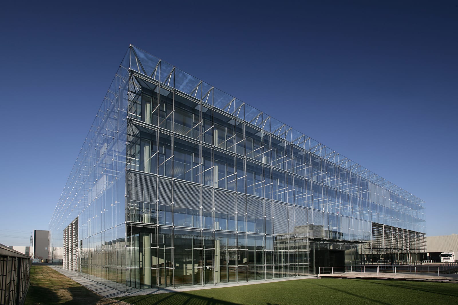 A long glass office building with an exposed steel frame under a clear blue sky, with a lawn in front, at Hugo Boss's headquarters in Metzingen, Germany