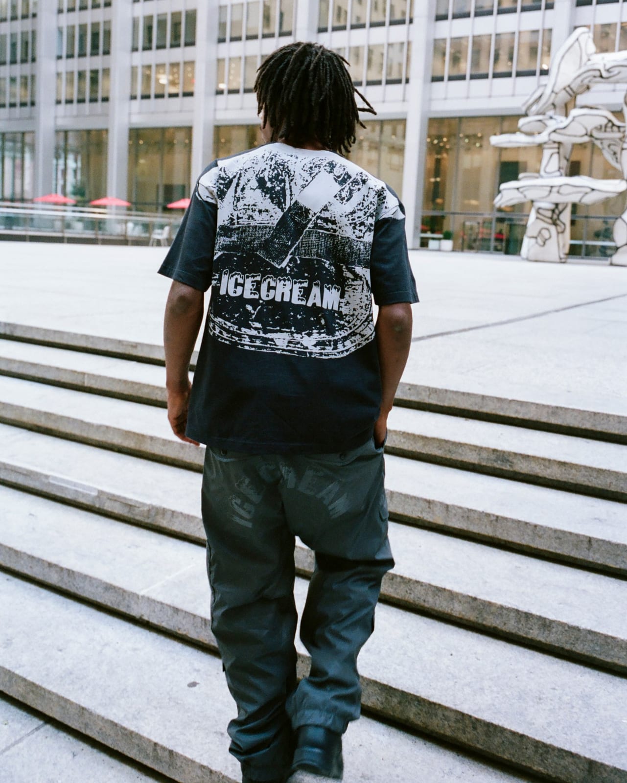 The back of a black T-shirt printed with a high-contrast reflective graphic and the ICECREAM wordmark, worn with pale reflective pants on stone steps at night