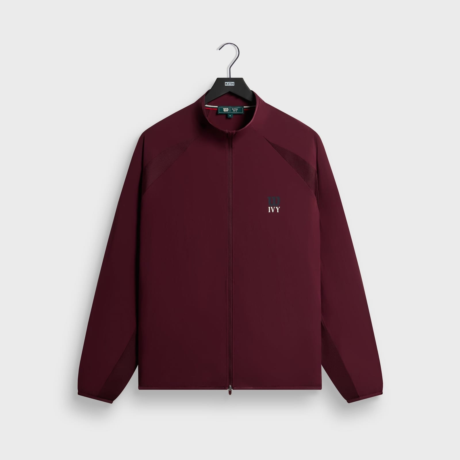 The Kith Ivy for Wilson classic warm-up jacket in Magma, a burgundy stand-collar zip jacket with mesh panels at the shoulders and a small Wilson W and Ivy mark on the chest, on a Kith hanger