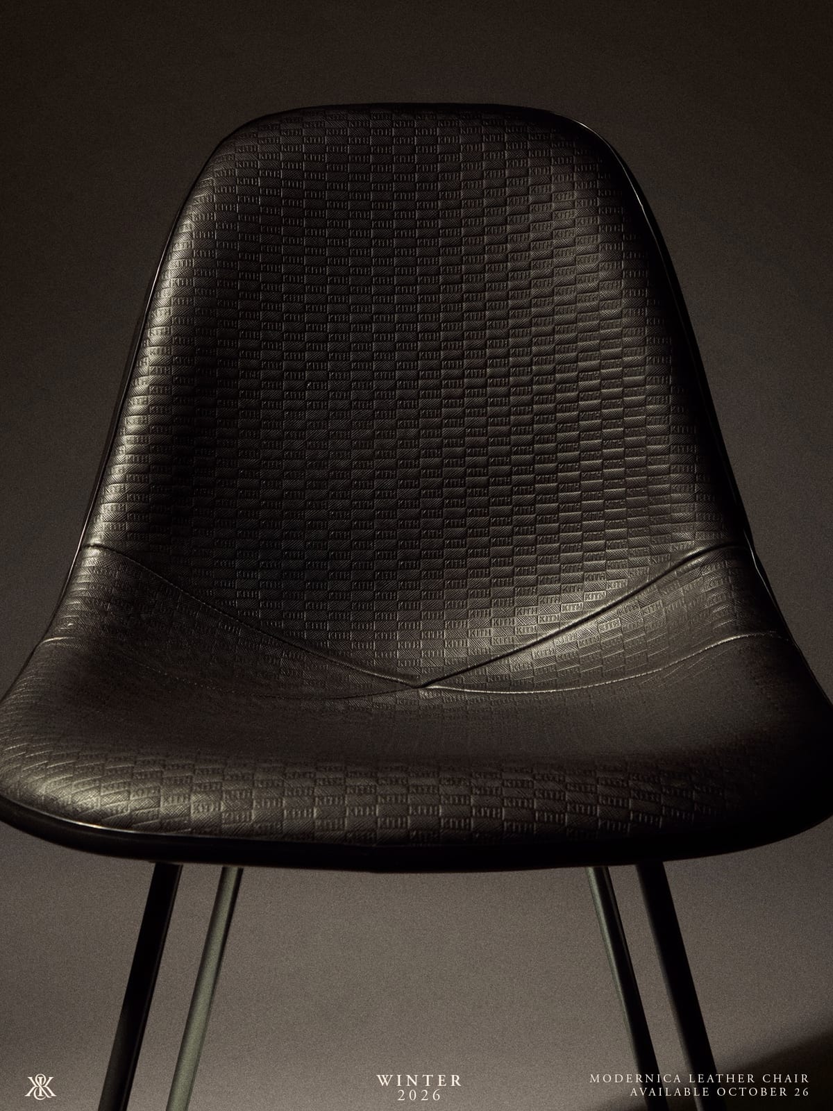 A black leather-covered moulded shell chair on thin black metal legs, lit from the side against a grey backdrop