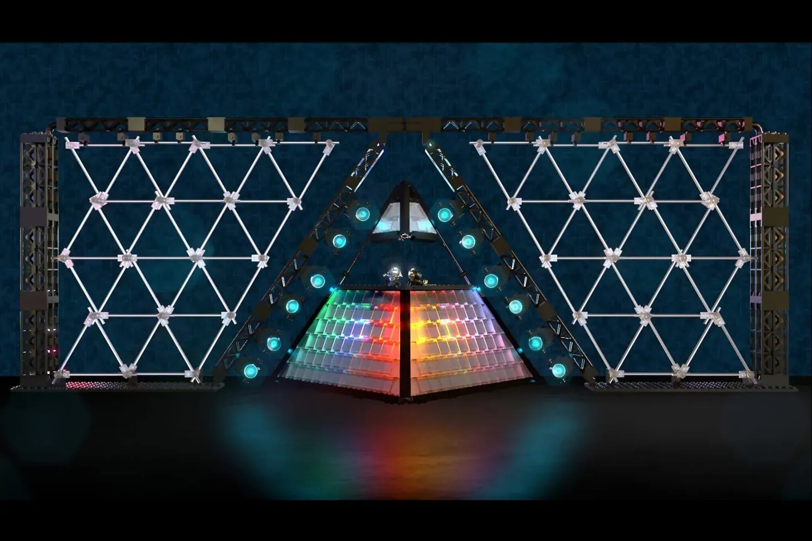 The fan-built LEGO model of Daft Punk's Alive 2007 pyramid stage: a glowing pyramid in rainbow-lit panels at the centre, flanked by two large lattice walls of white triangles on black scaffolding, against a dark blue backdrop