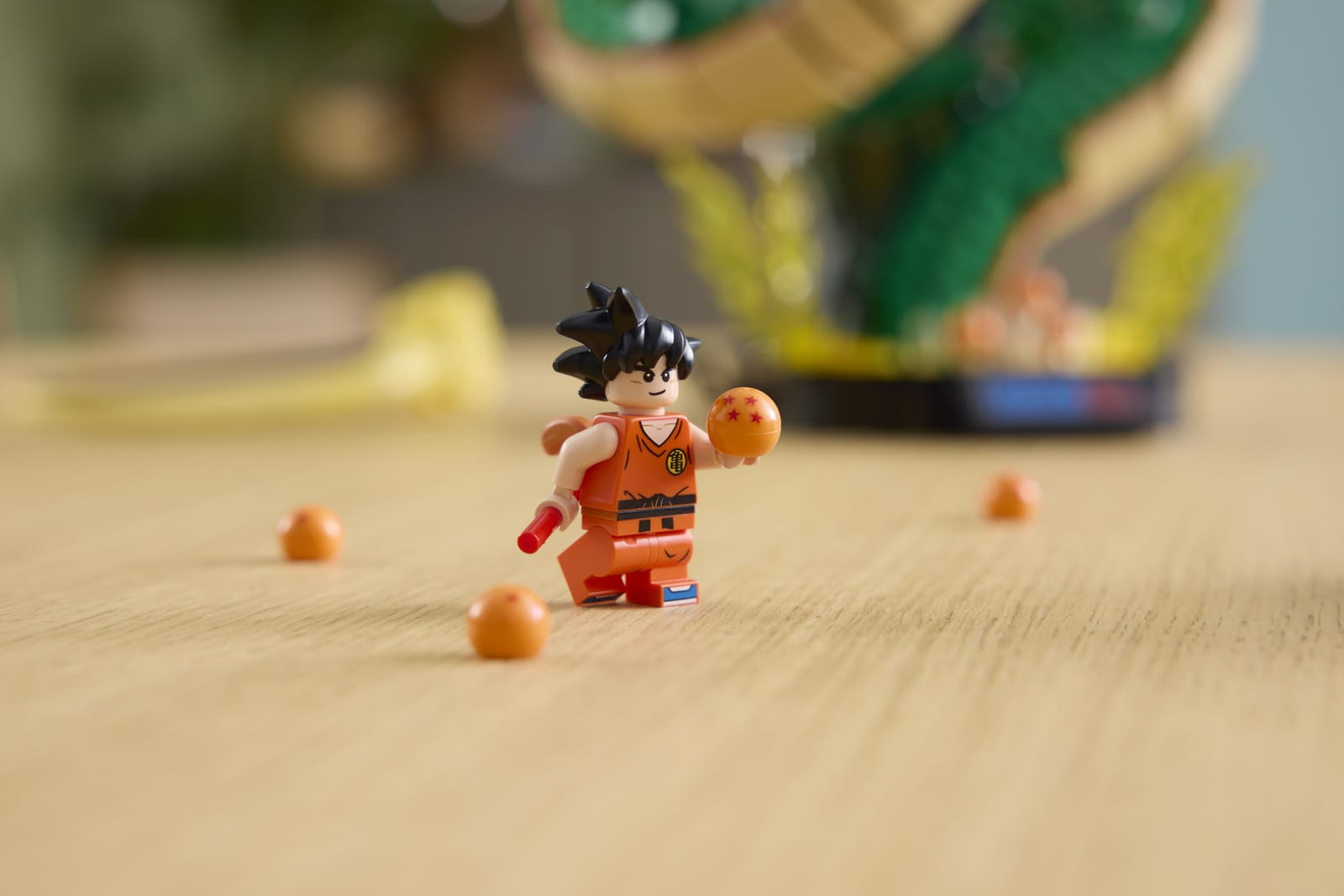 The Kid Goku minifigure from the LEGO Dragon Ball Shenron & Goku set, holding an orange Dragon Ball on a wooden table, with the Shenron model blurred behind him