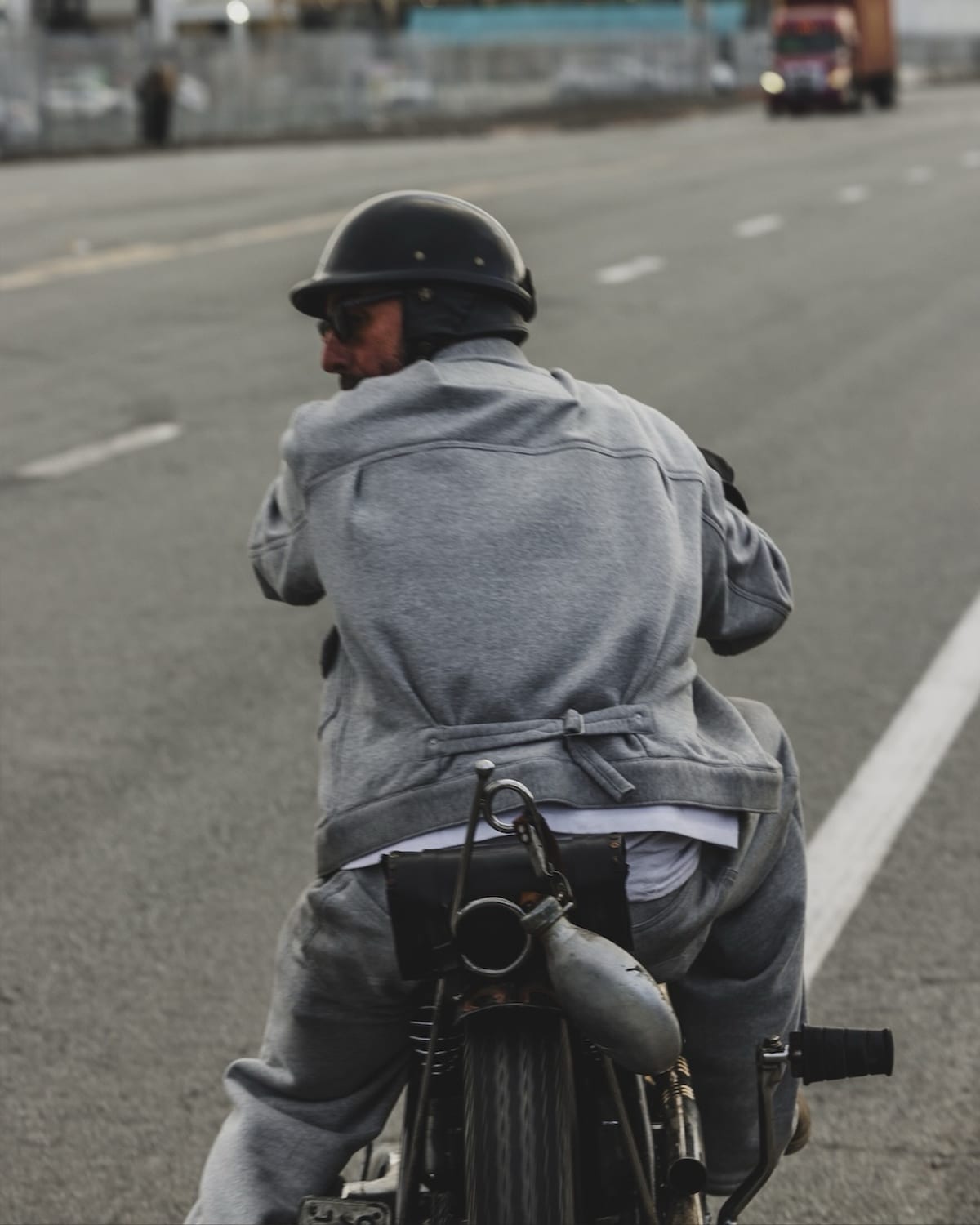 A rider seen from behind on a motorcycle on an open road, wearing the Heather Gray Super Wide Trucker and Super Wide Pant