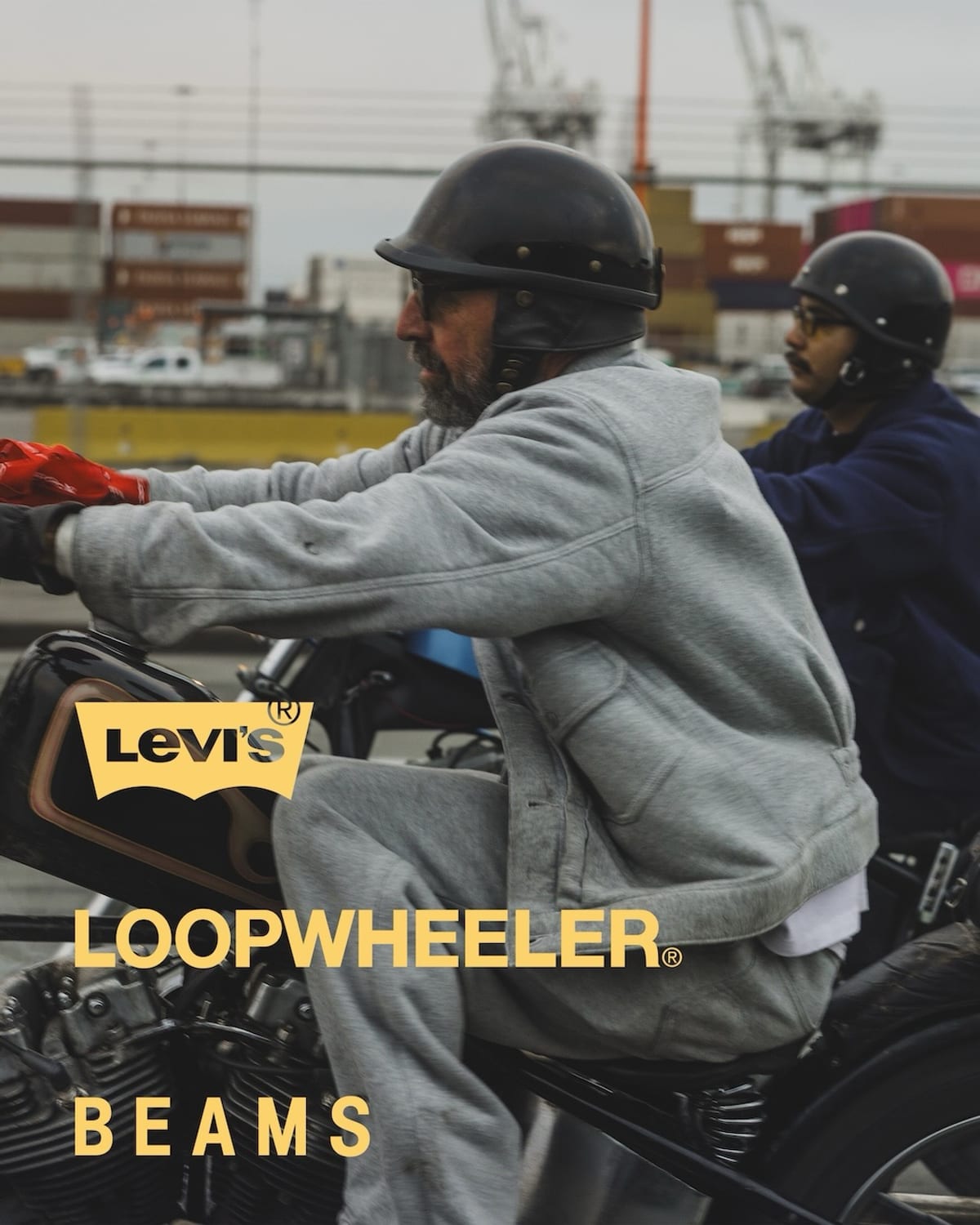 Two riders on motorcycles at a shipping port, one in the Heather Gray trucker and pant and the other in navy, with the Levi's, LOOPWHEELER and BEAMS logos over the photo