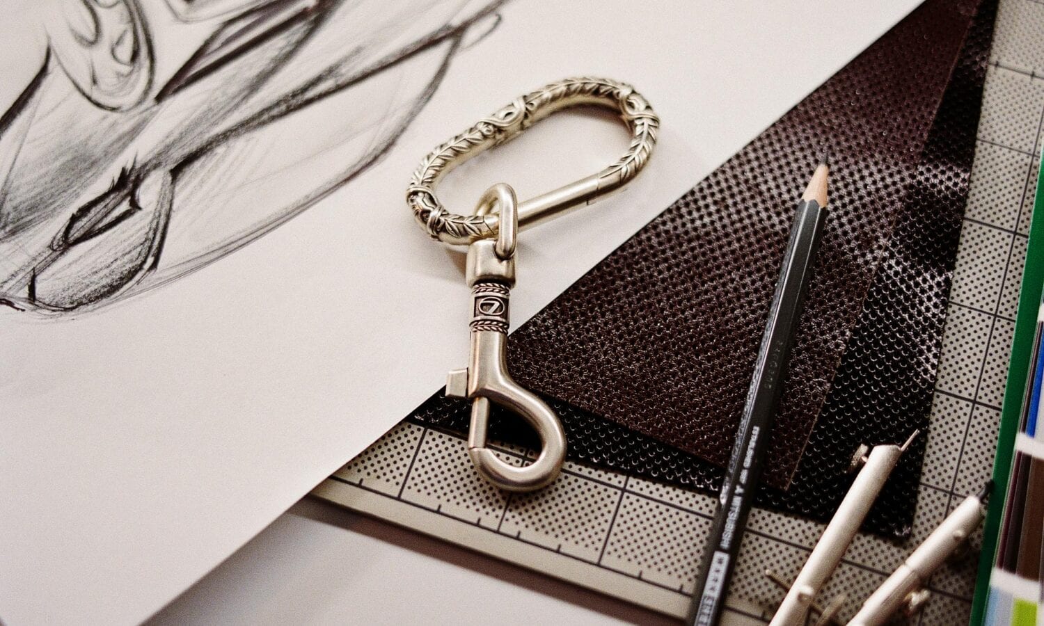 The Future Classic Club engraved chrome carabiner, resting on a leather swatch next to design sketches