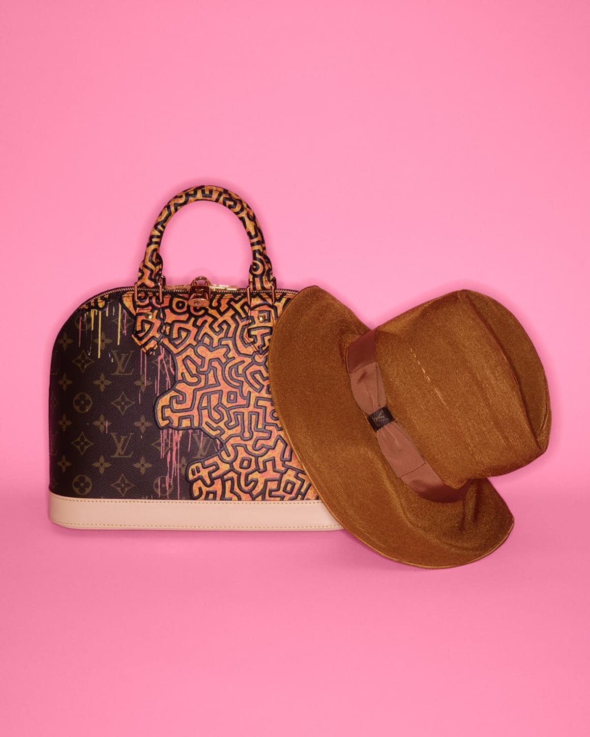 A Louis Vuitton Alma bag in monogram canvas overlaid with Keith Haring's black linework, shown on a pink background beside a brown felt hat, from the Cruise 2027 collection