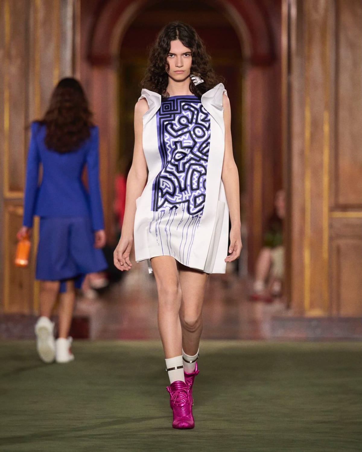A Cruise 2027 look at the Frick Collection: a white dress with a panel of Keith Haring's blue linework, worn with socks and pink boots