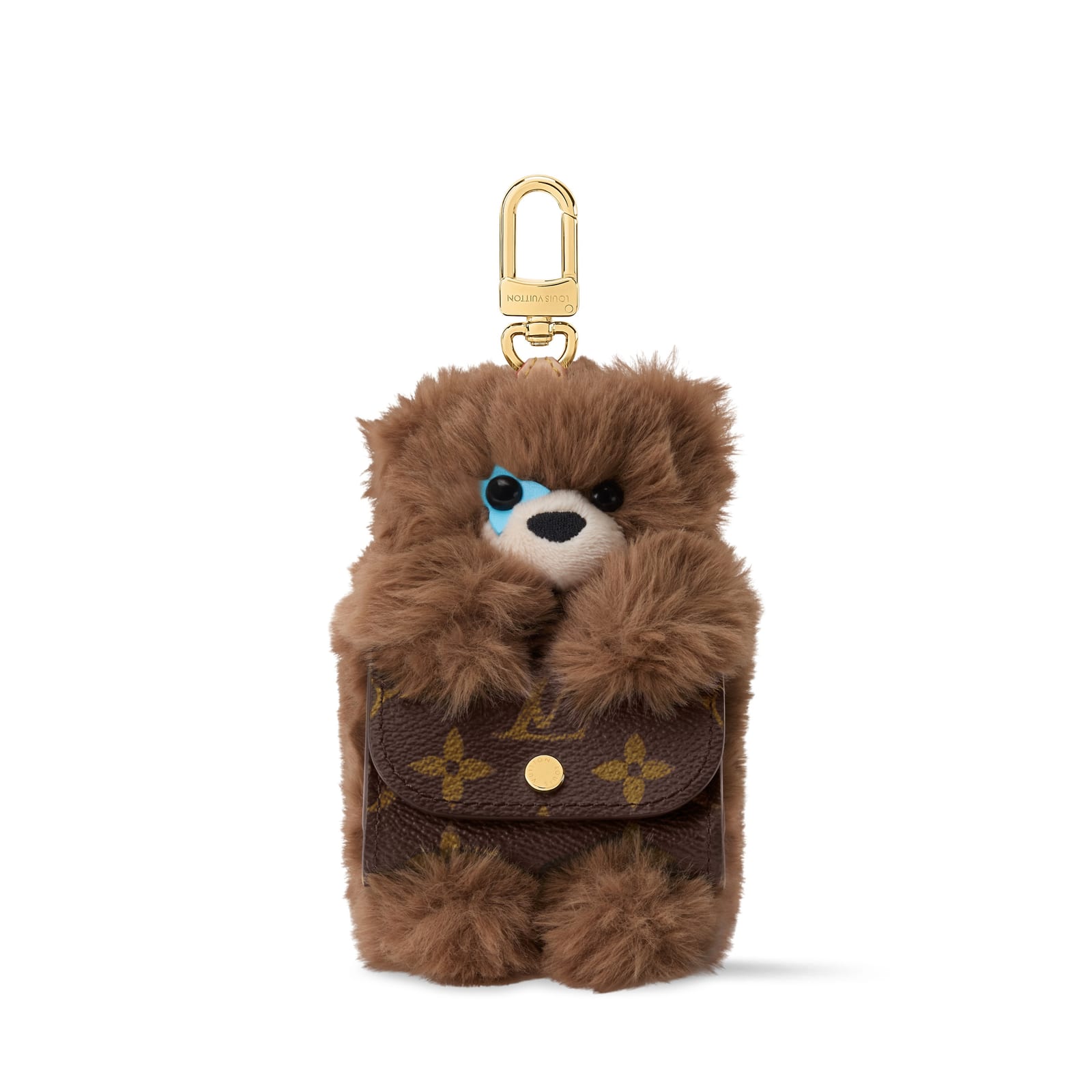 A brown furry teddy bear charm with black eyes and a light blue patch around one, holding a small Monogram canvas pouch in its paws, hanging from a gold clasp