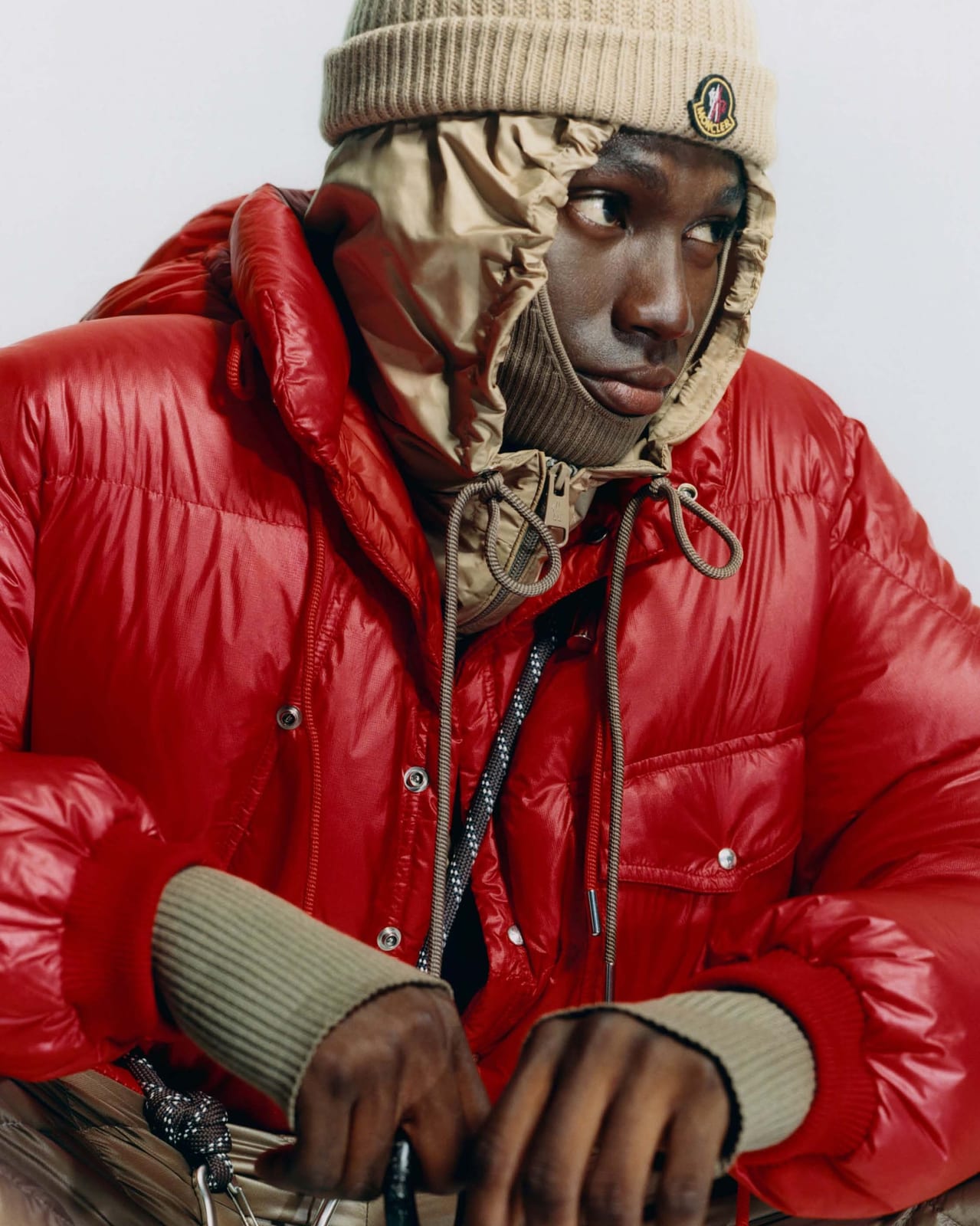 A model in Moncler's new Re/Icons Karakorum jacket in glossy red, with a tan hood lining and a knit beanie with the Moncler patch
