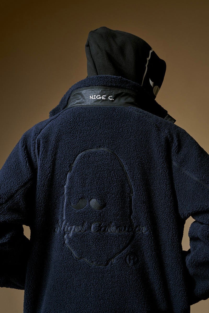 The back of a navy pile fleece with a large ape head and a Nigel Cabourn script logo worked tone-on-tone into the pile, under a black hood with a NIGE C. label at the collar