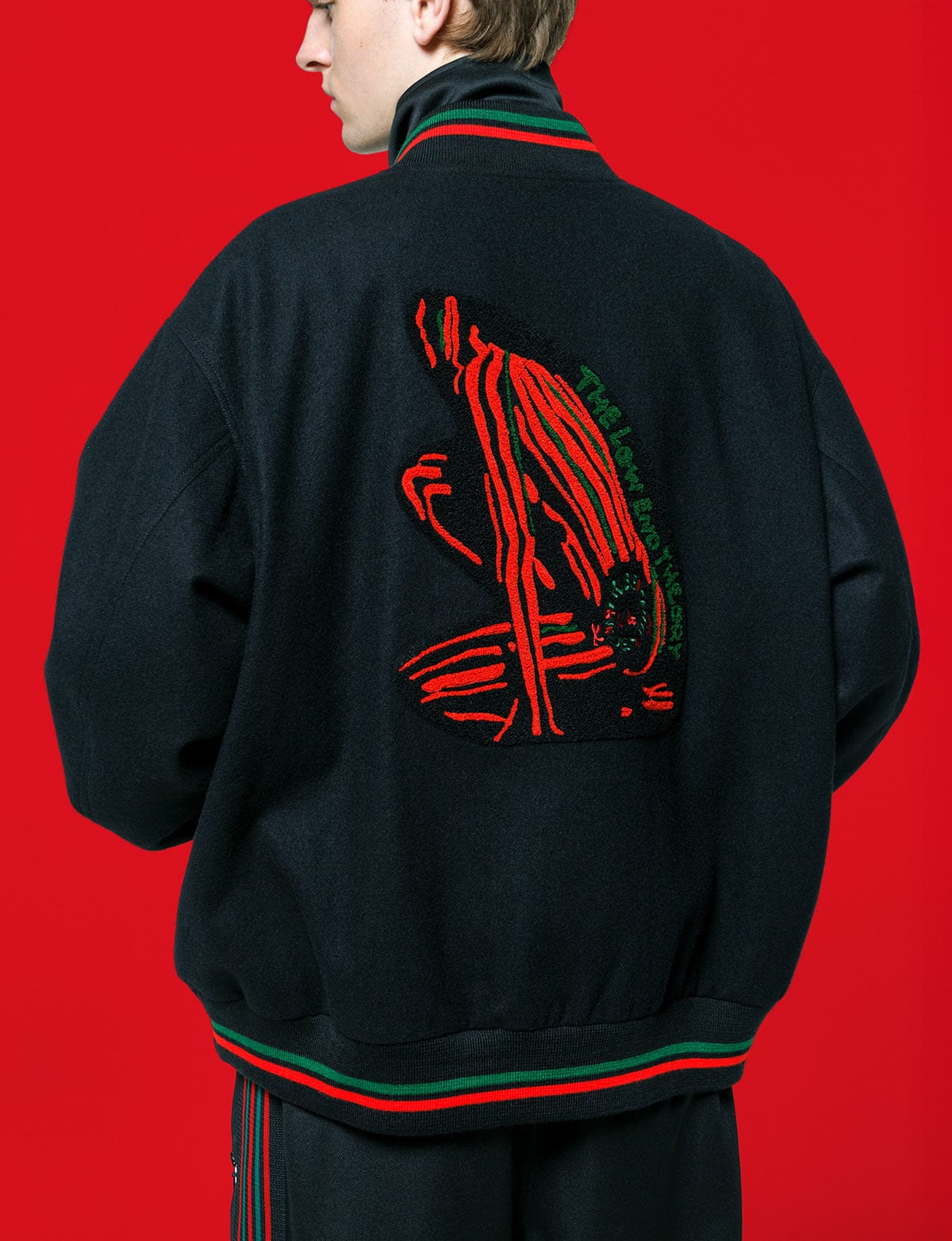 The back of the Needles x A Tribe Called Quest B.B. Jacket in black, with the red and green figure from The Low End Theory's cover and the group's name in green, against a red backdrop