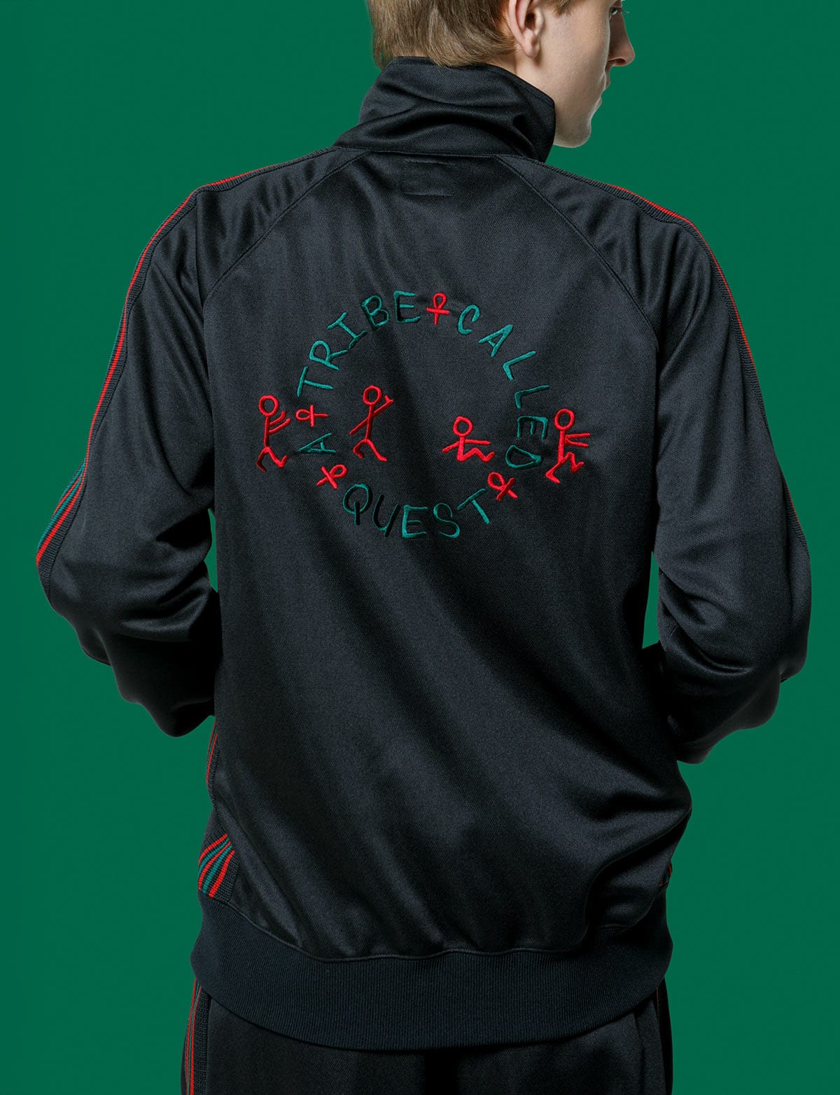 The back of the Needles x A Tribe Called Quest Track Jacket in black, with red and green stripes on the sleeves and A Tribe Called Quest's circular logo embroidered in red and green, against a green backdrop