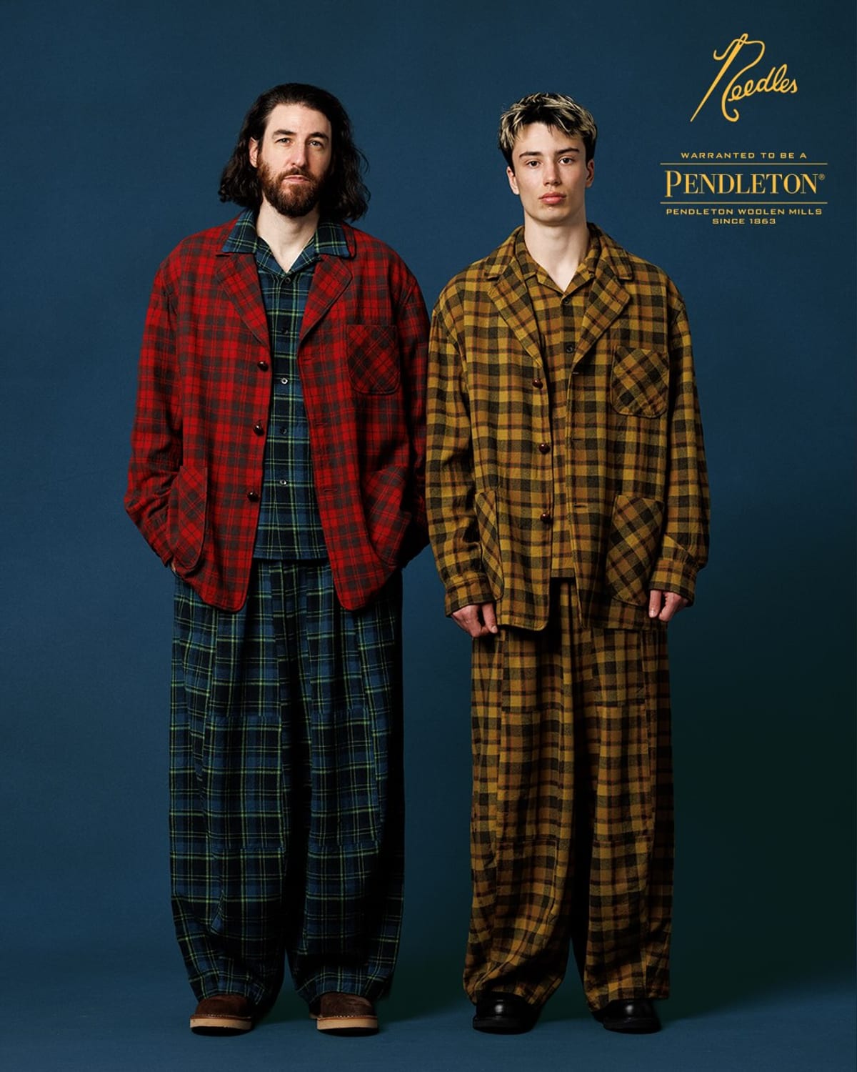 Two models in the Needles x Pendleton Pen Jacket, one in red plaid over a matching blue and green plaid shirt and trousers, one in a matching mustard plaid jacket and trousers, against a navy backdrop