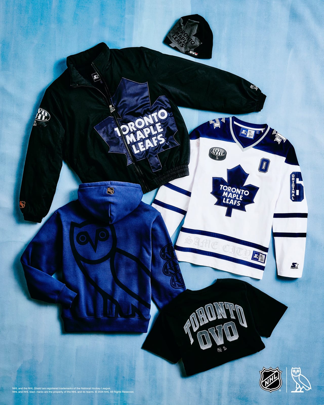 The Toronto Maple Leafs set laid flat on a pale blue backdrop: a black Starter nylon jacket with a big satin maple leaf crest, a white and blue long-sleeve hockey top with the leaf crest, a blue hoodie with a large tonal OVO owl on the back, a black tee reading TORONTO OVO, and a black knit beanie