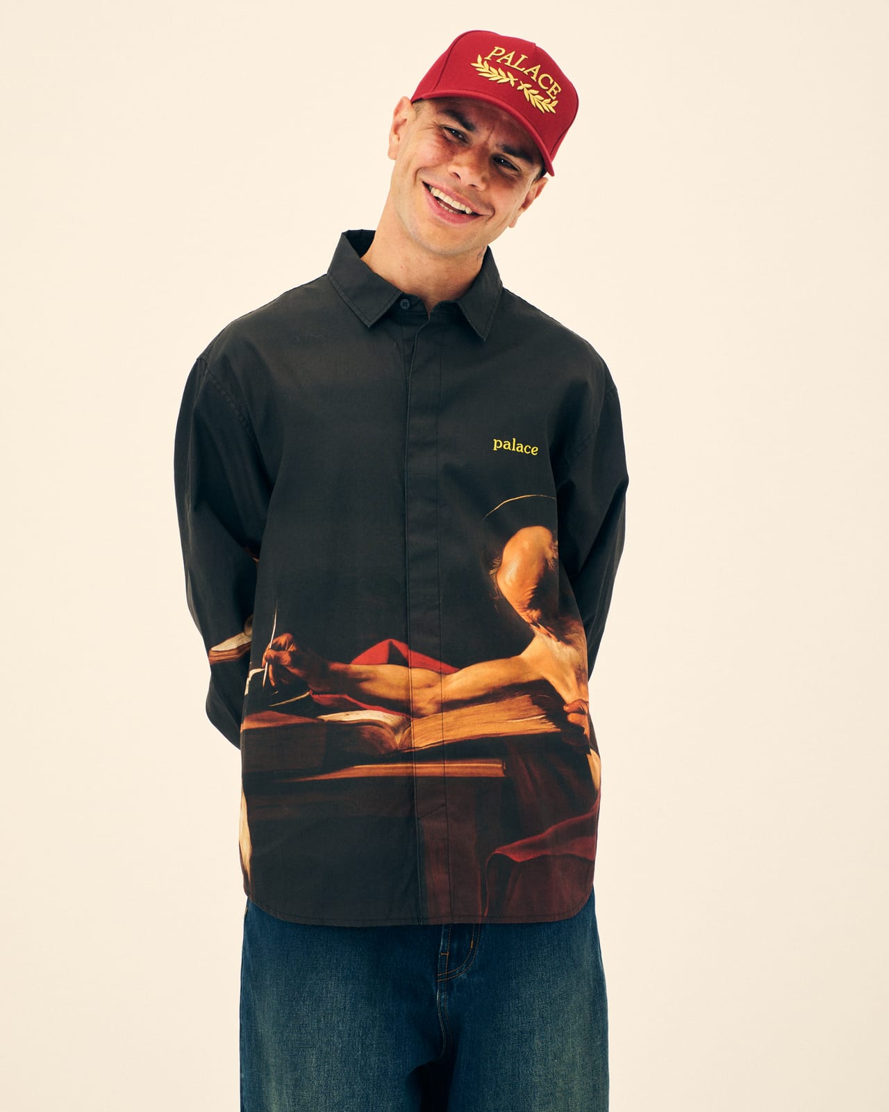 A Palace Winter 2026 button-up shirt printed with Caravaggio's Saint Jerome Writing, worn with a red Palace cap
